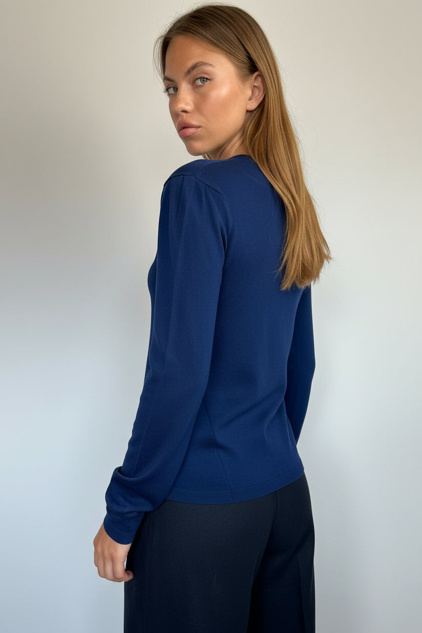 A woman wearing a navy blue long-sleeve crewneck top, shown from a side profile against a plain light gray wall.