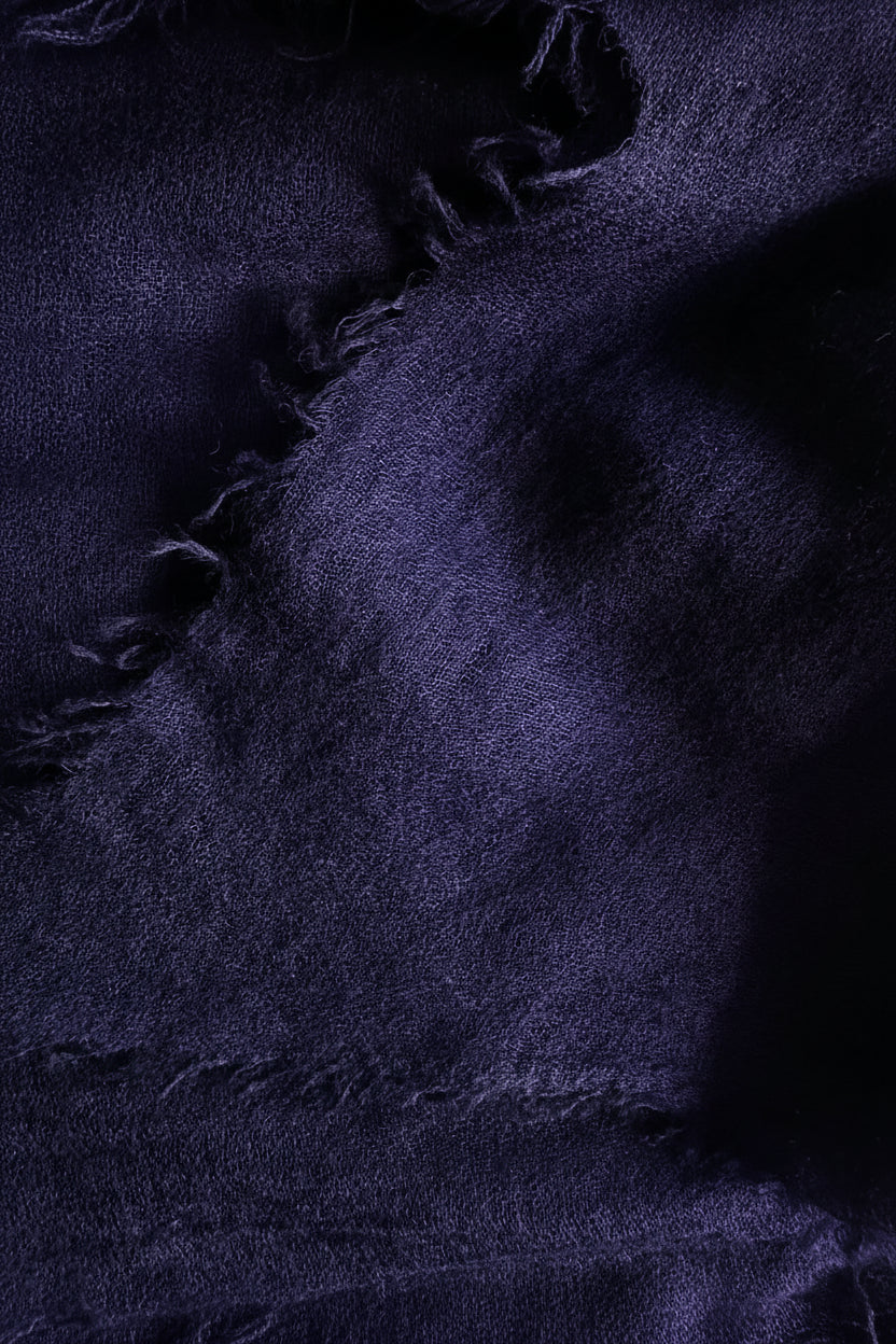 A close-up of a textured purple fabric with a frayed, tattered edge and a mottled, shimmering surface.