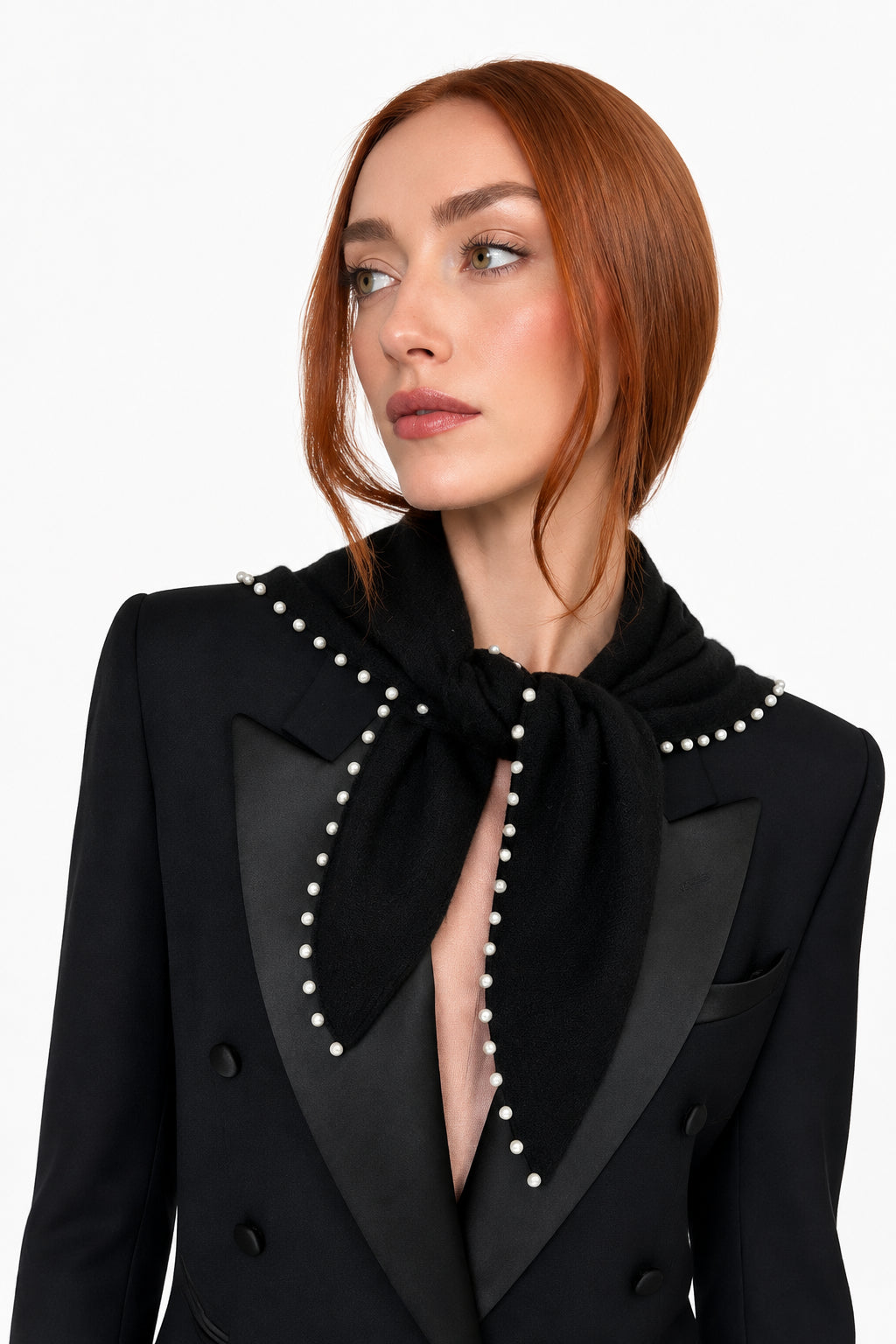 A woman with red hair wearing a black velvet scarf with white pearl-like trim, styled over a black blazer and a pink top, photographed against a plain light background.