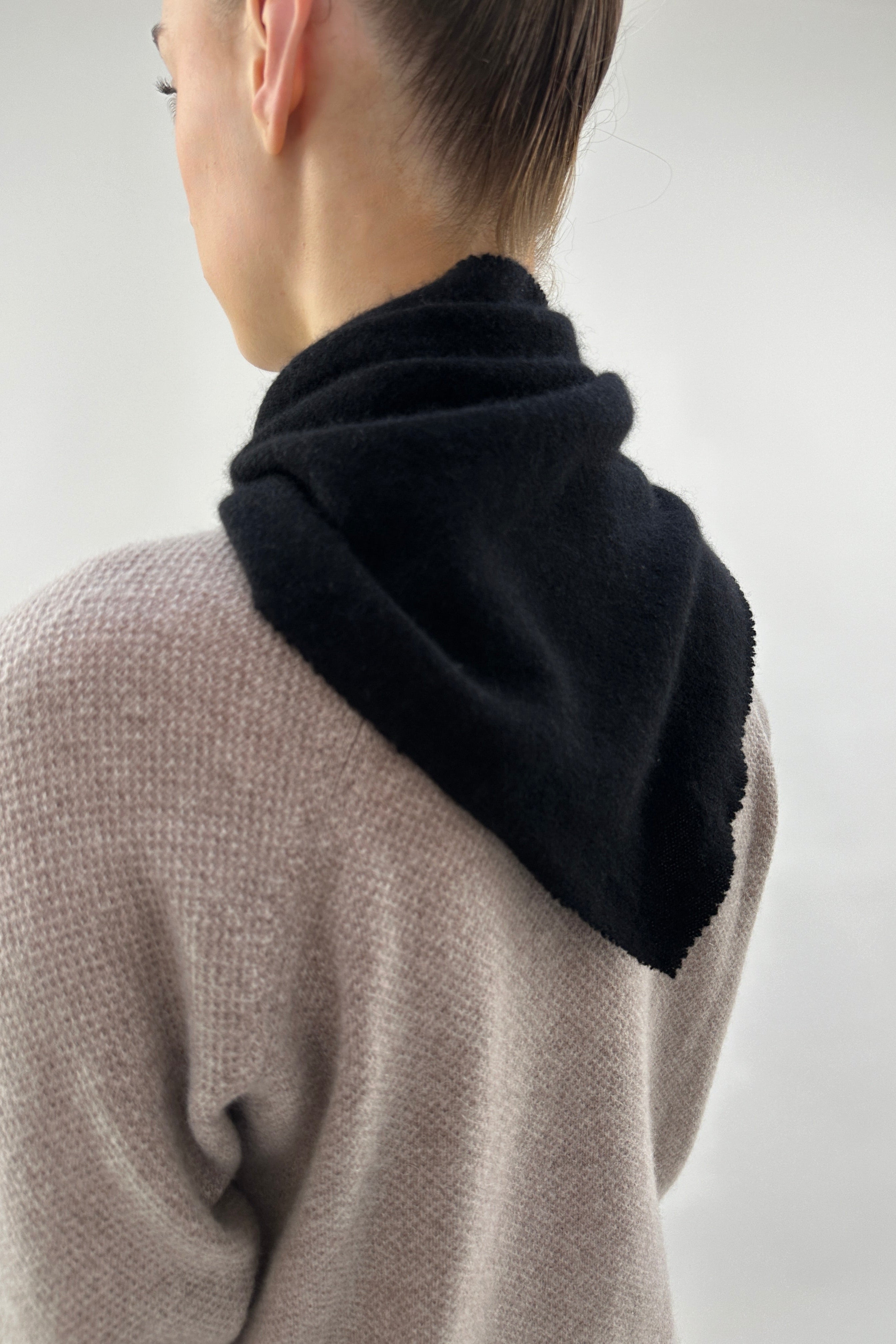 Person wearing a black scarf over a beige sweater on a plain background