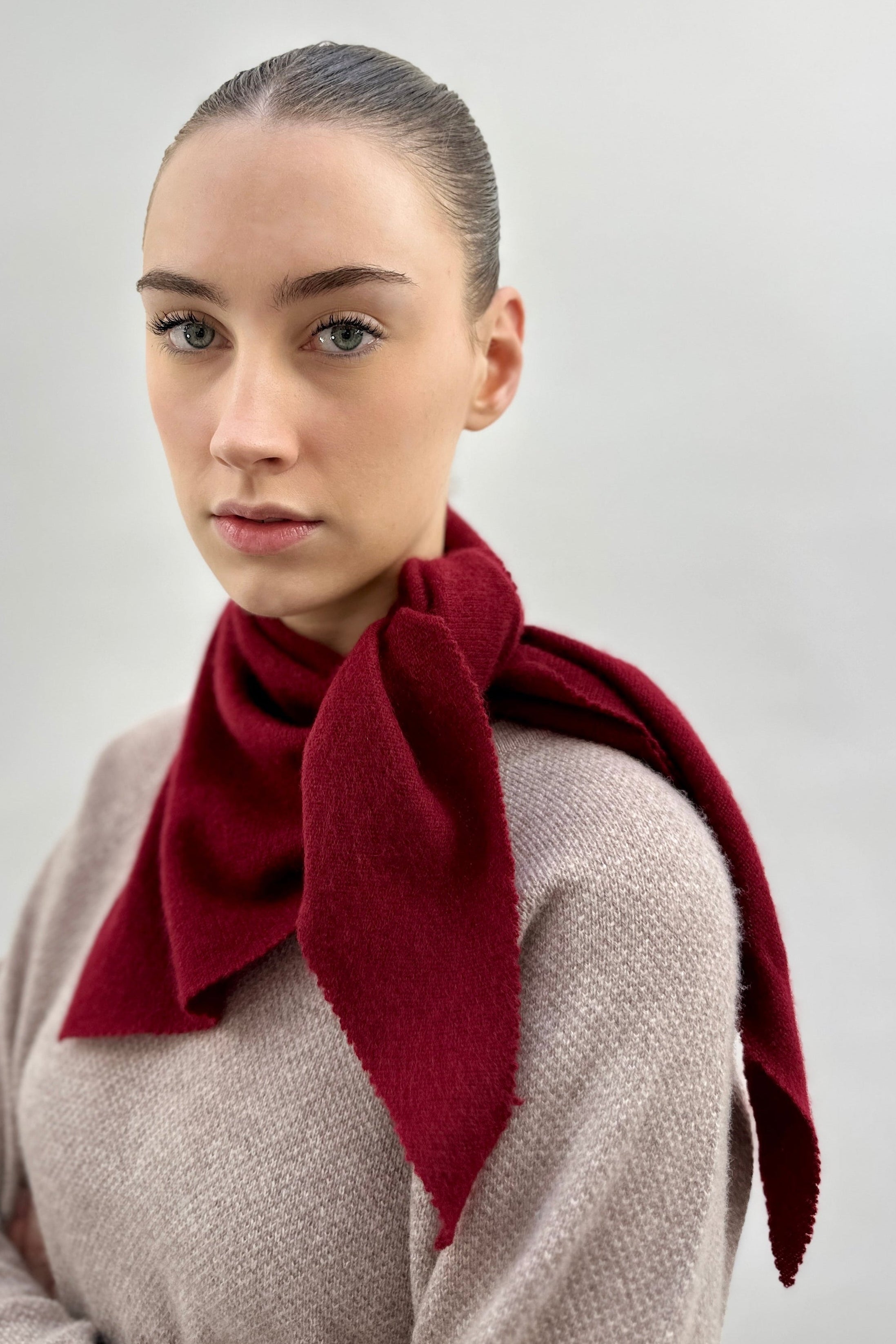 Woman wearing a claret scarf around her neck against a plain background
