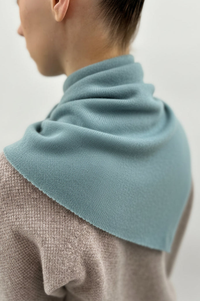 Person wearing a blue scarf over a beige sweater on a plain background