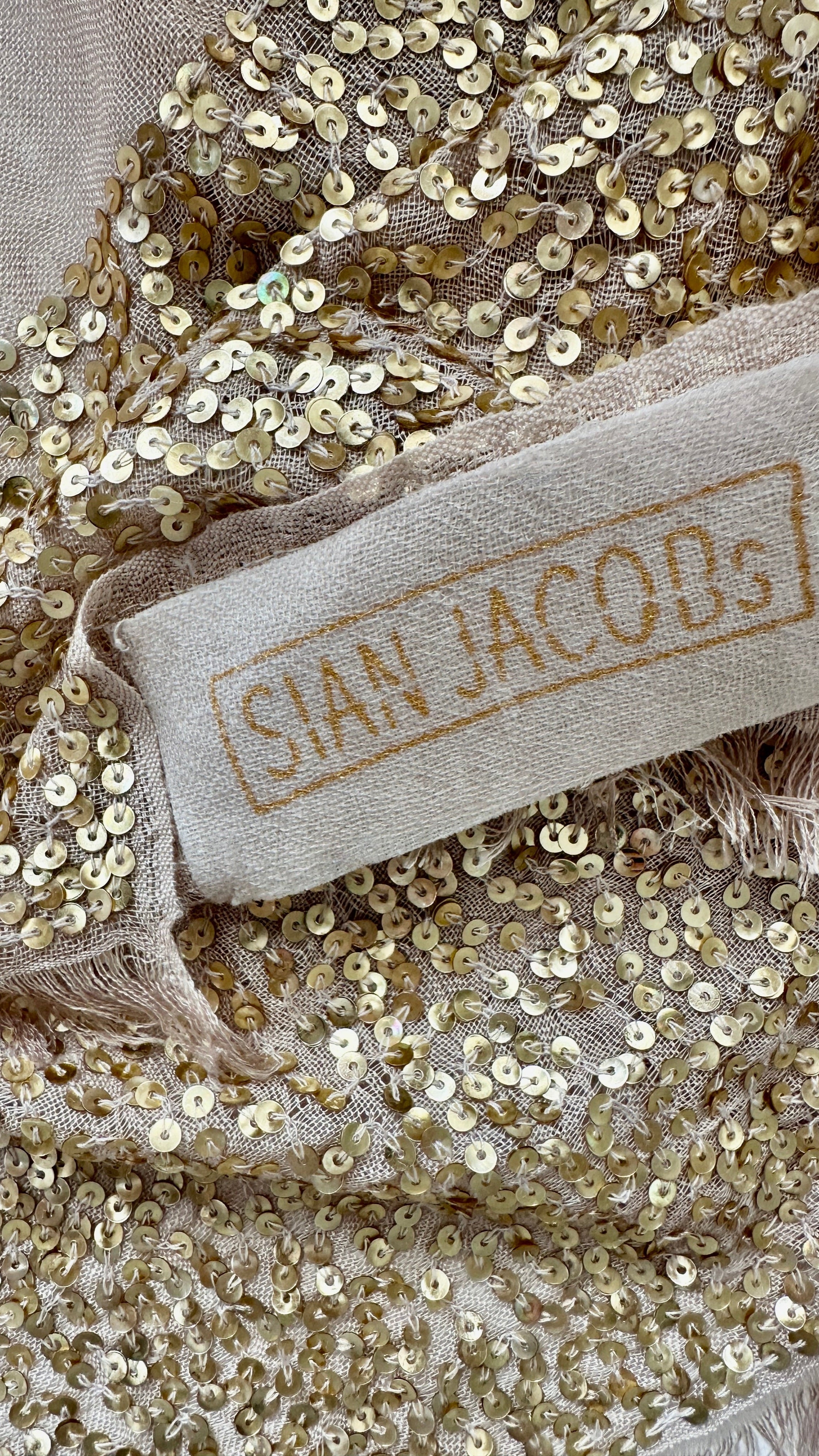Close-up of gold sequin fabric with a 'Sian Jacobs' label.