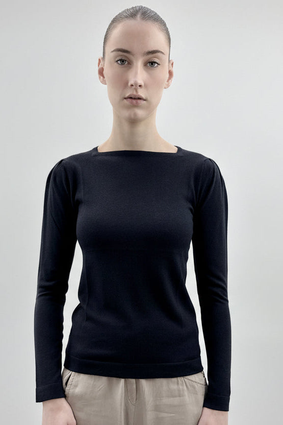 Person wearing a black long-sleeve top against a plain background