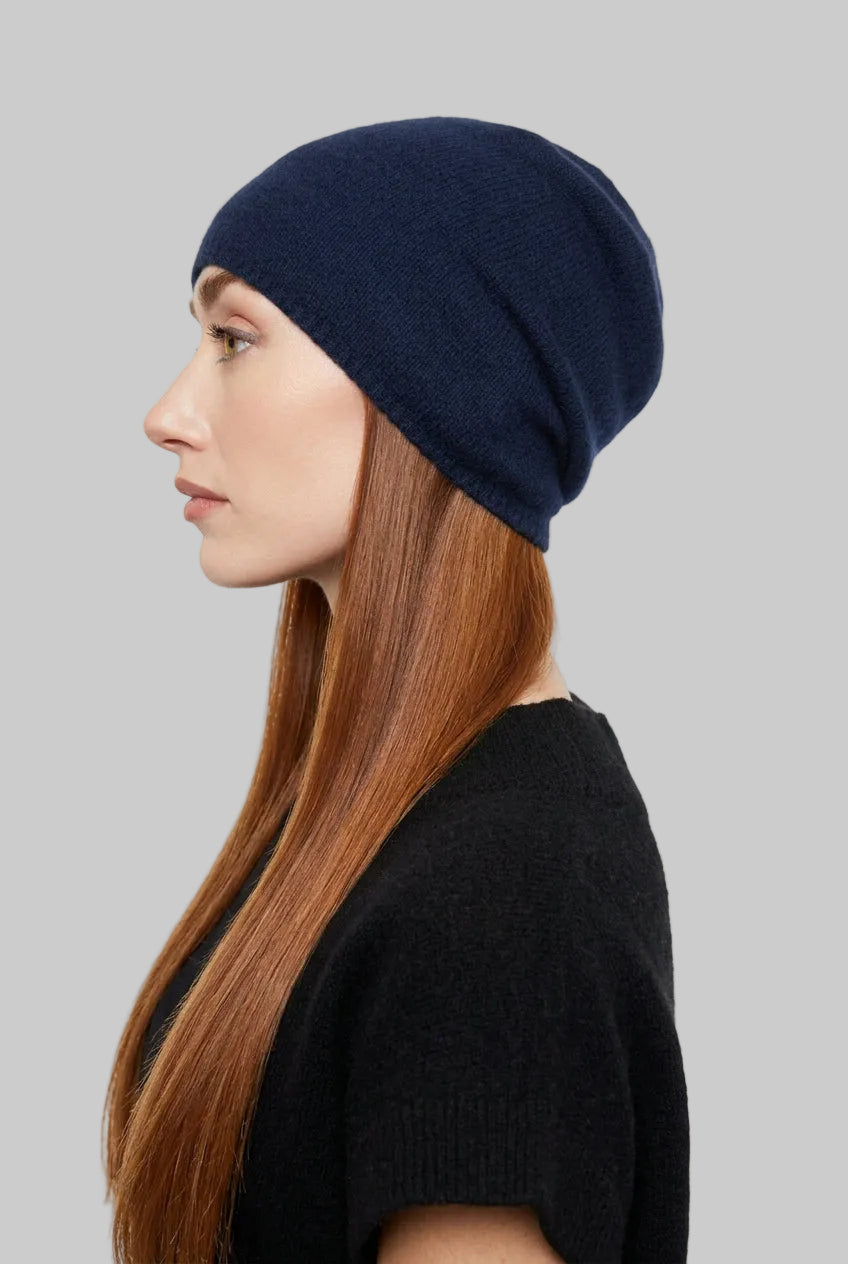 A woman in profile wearing a dark navy blue knit beanie and a black knit top, photographed against a plain light background.