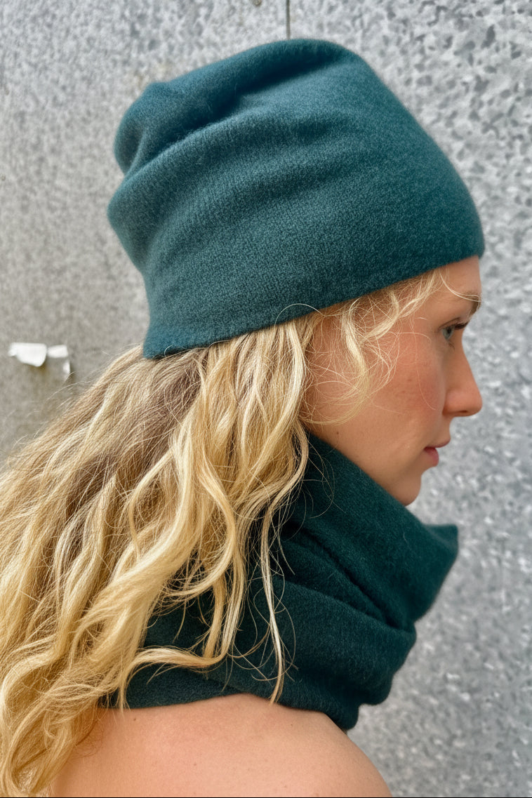 woman wearing a teal beanie and scarf against a textured wall