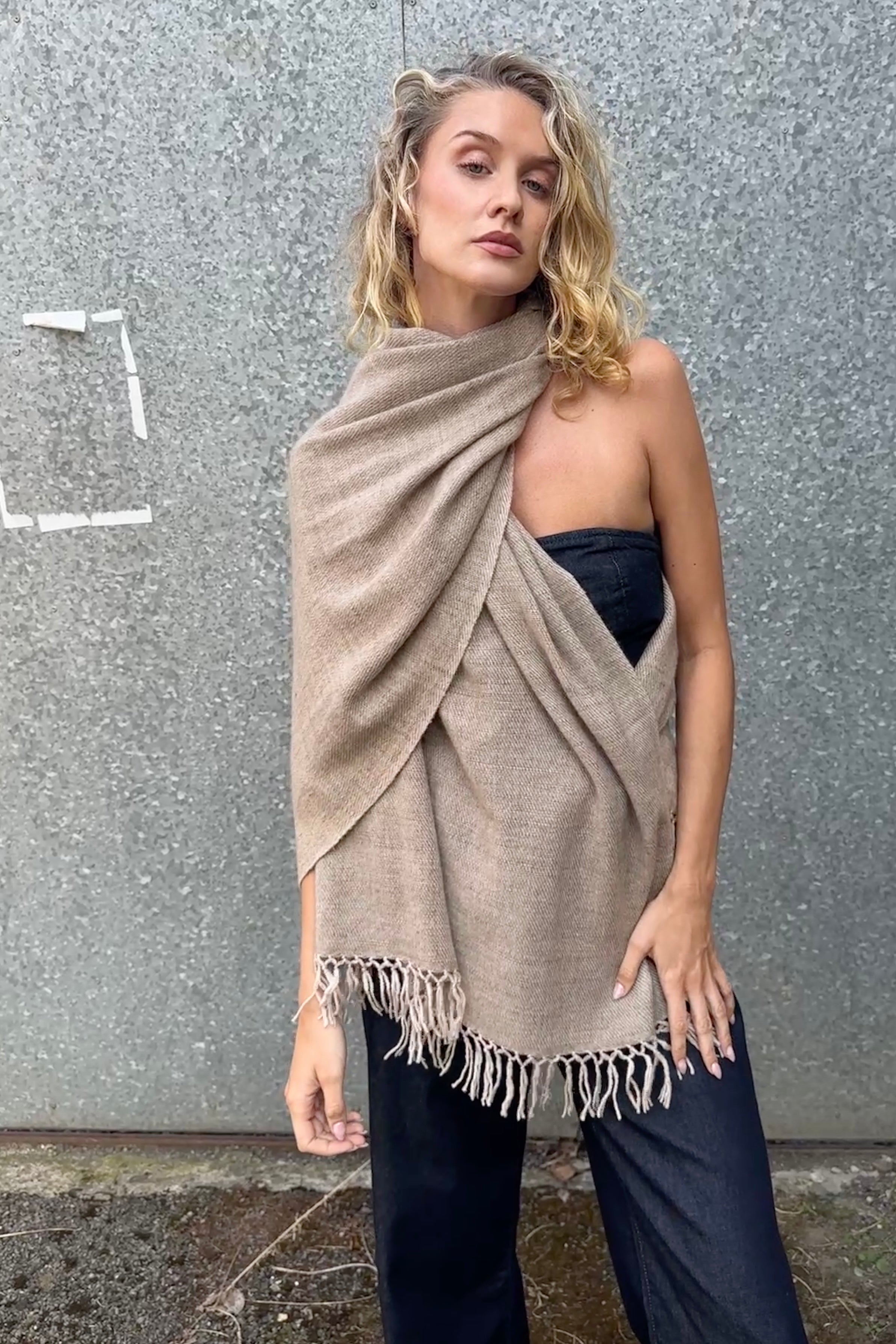 model wearing a beige cashmere blanket shawl with fringes against a gray background