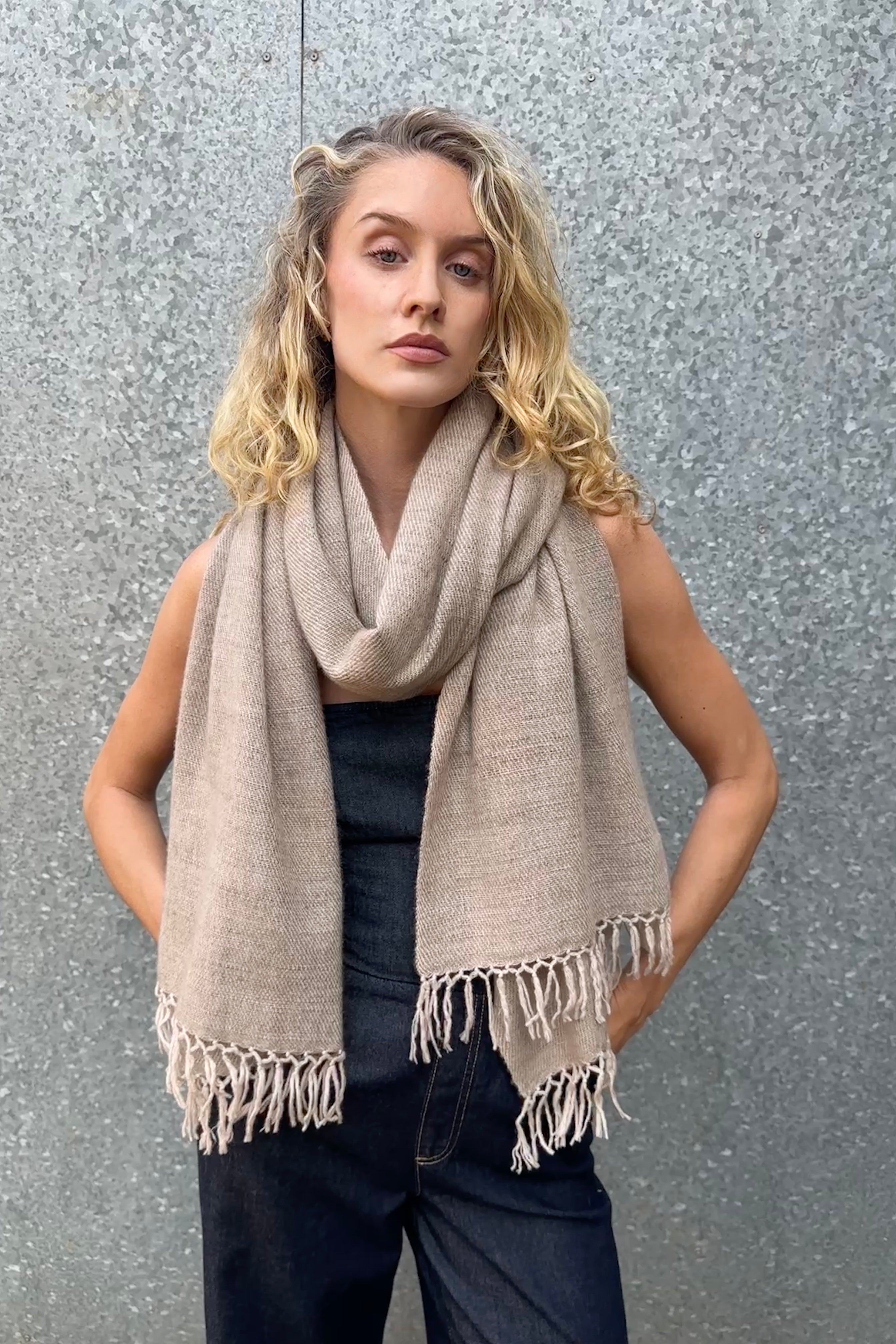 model wearing a beige cashmere blanket shawl with fringes against a gray background