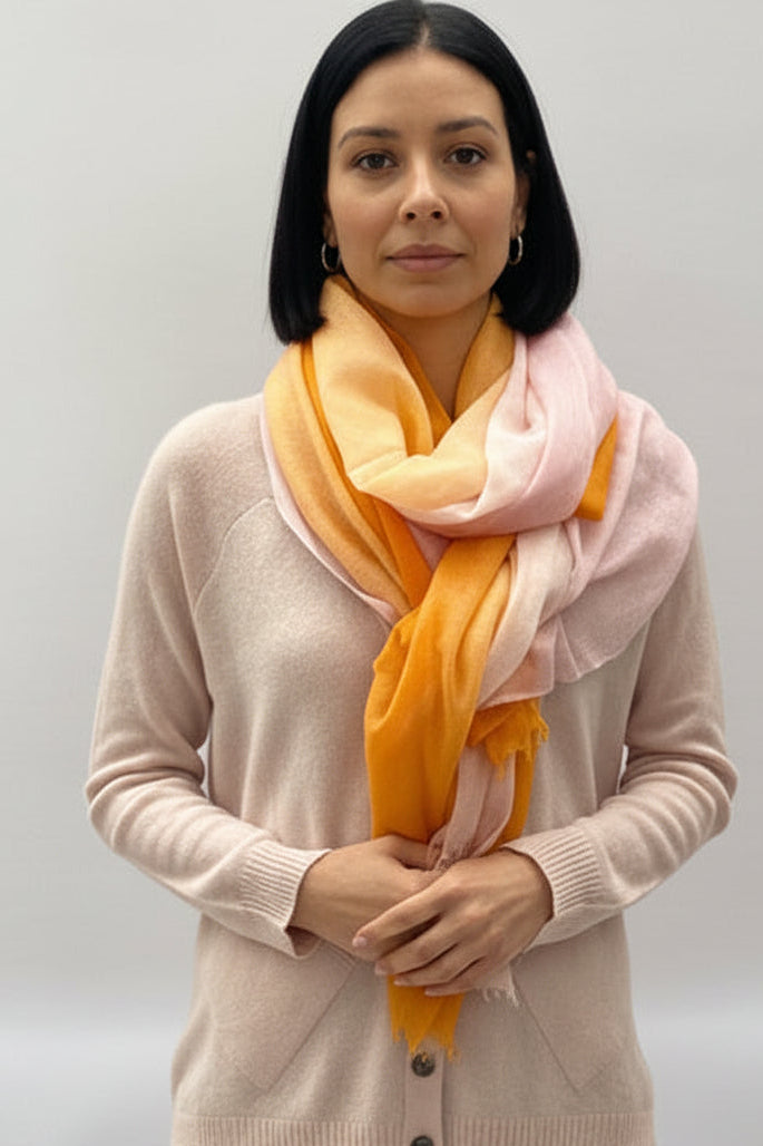 Woman wearing an ombre pink orange carf against a plain background