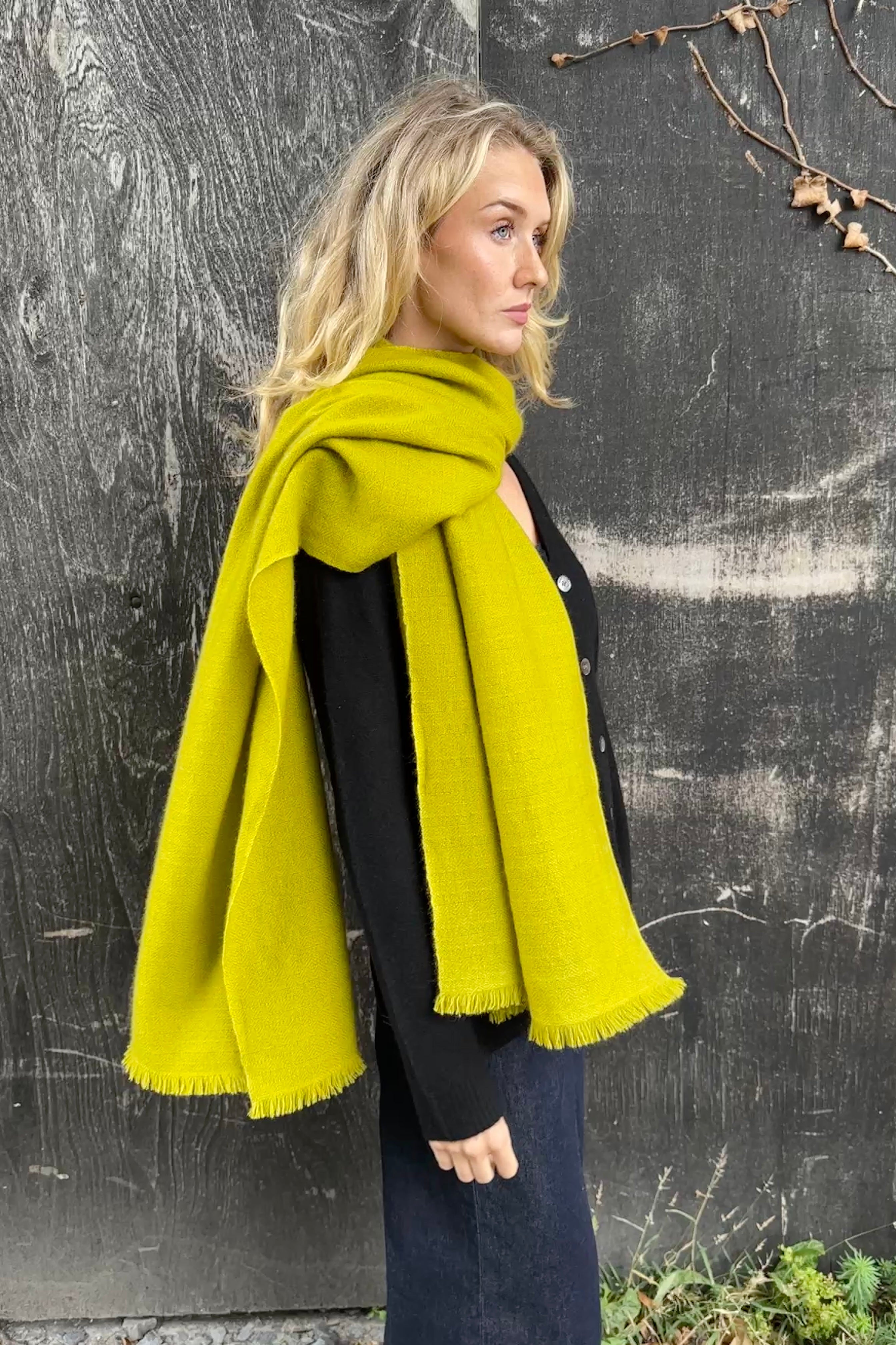 model wearing a bright yellow green cashmere kitty tumeric scarf against a dark background side view
