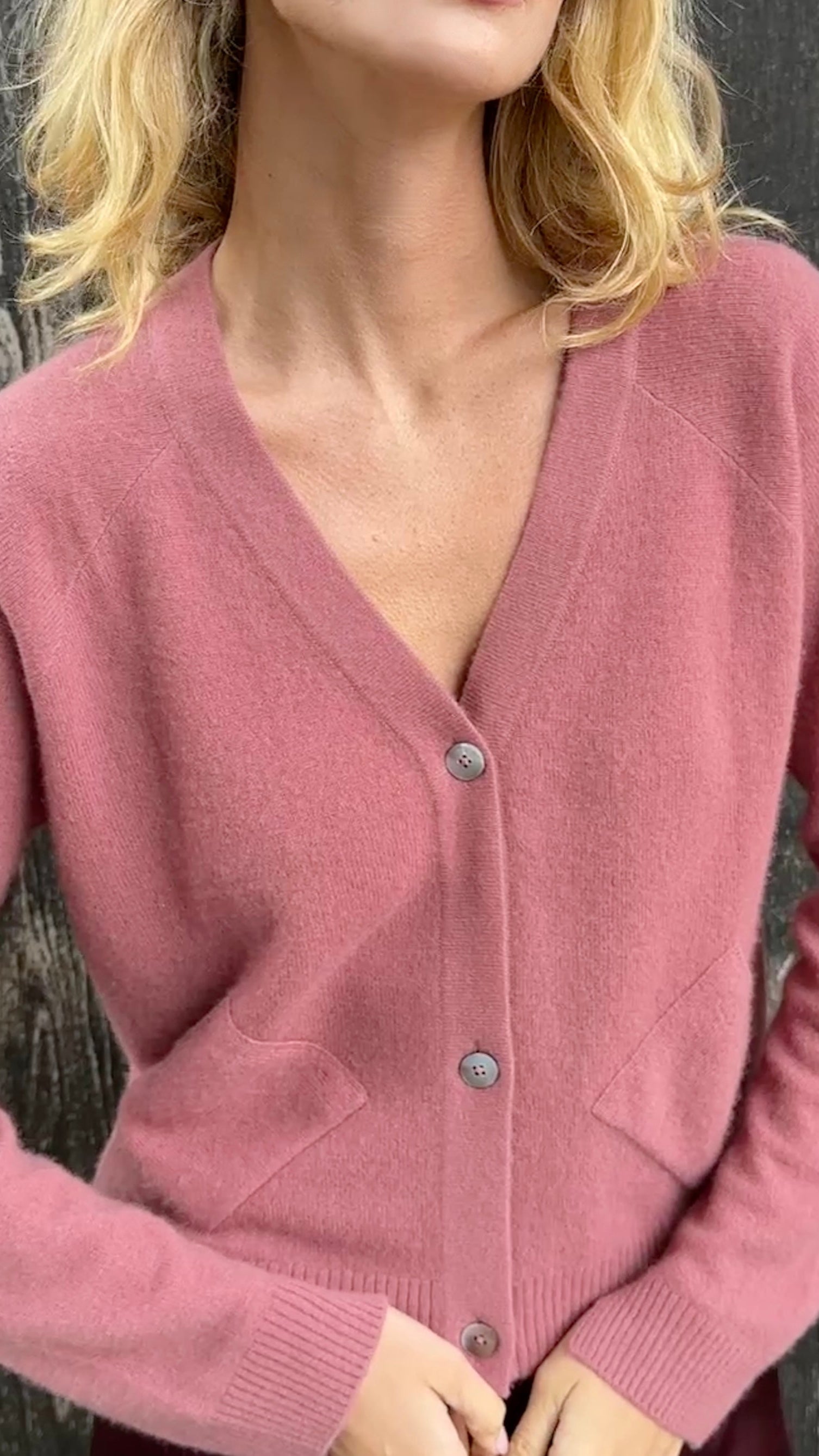 model wearing a zola rose pink cardigan against a textured dark background close up