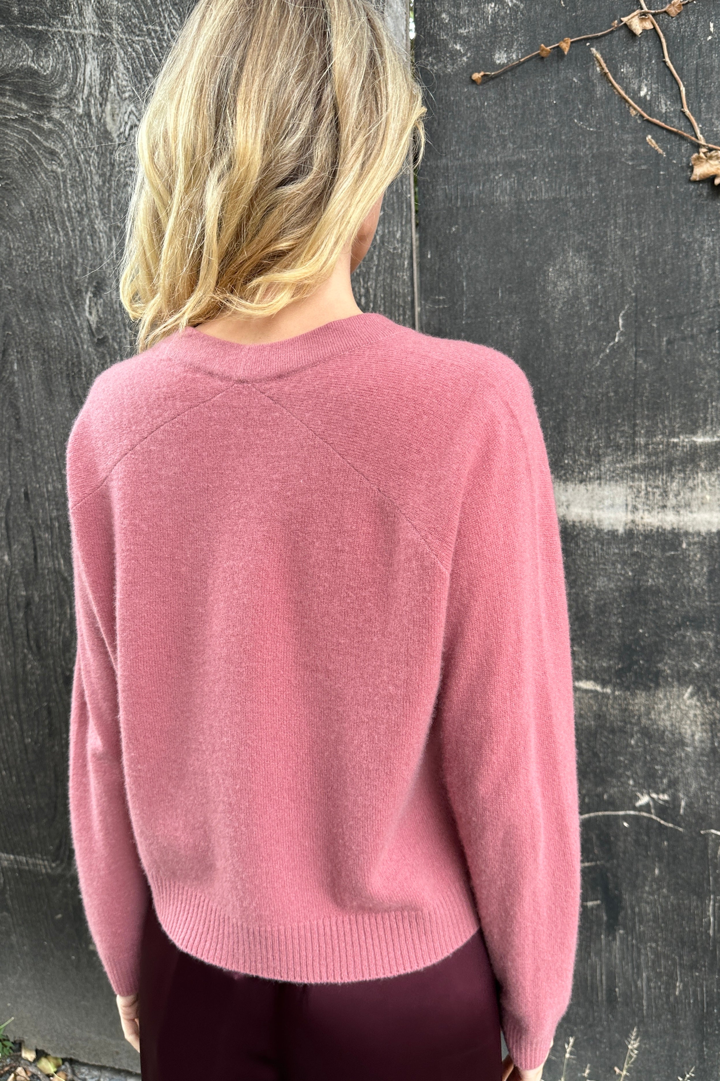 model wearing a zola rose pink cardigan against a textured dark background back view