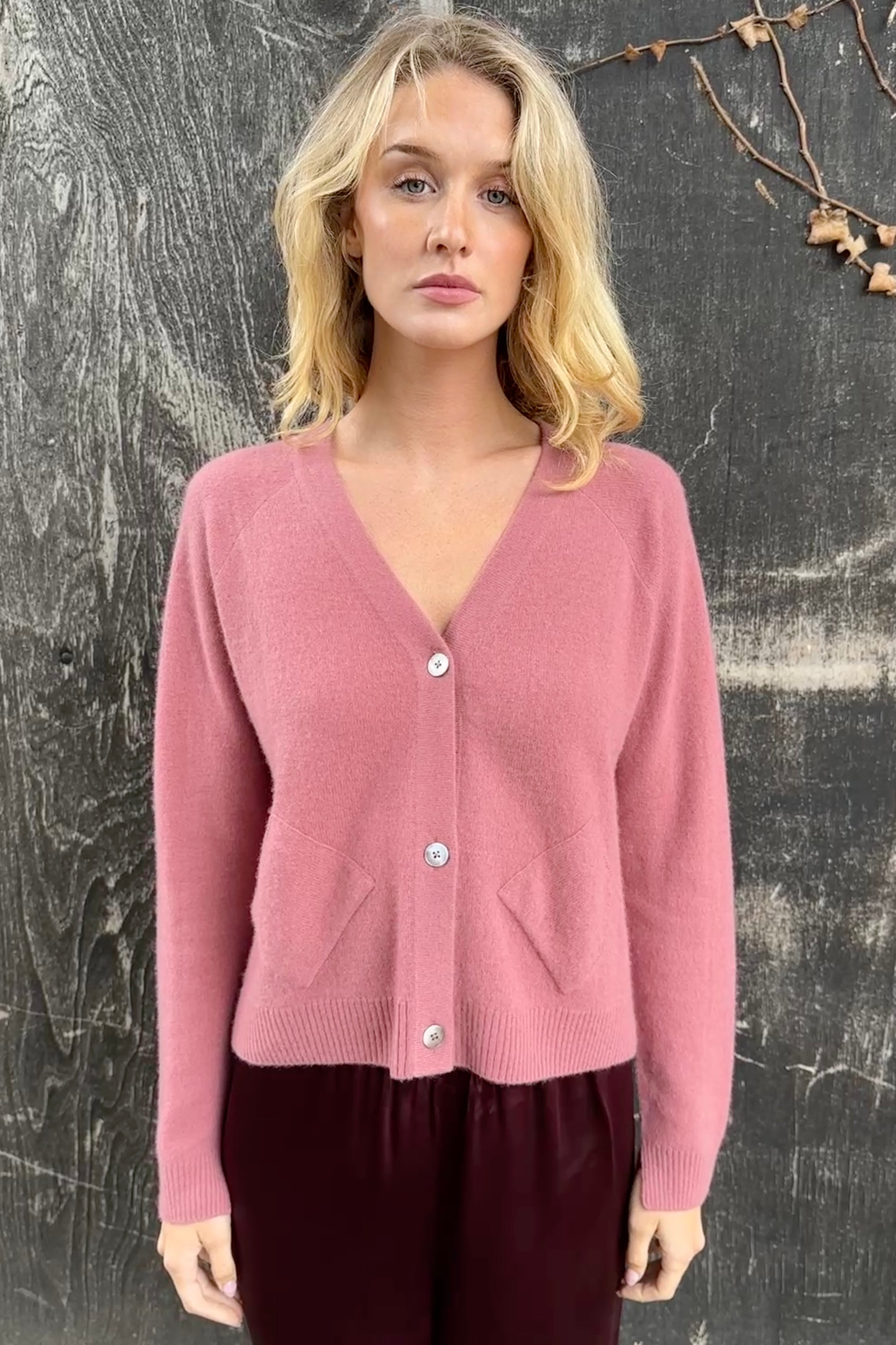 model wearing a zola rose pink cardigan against a textured dark background
