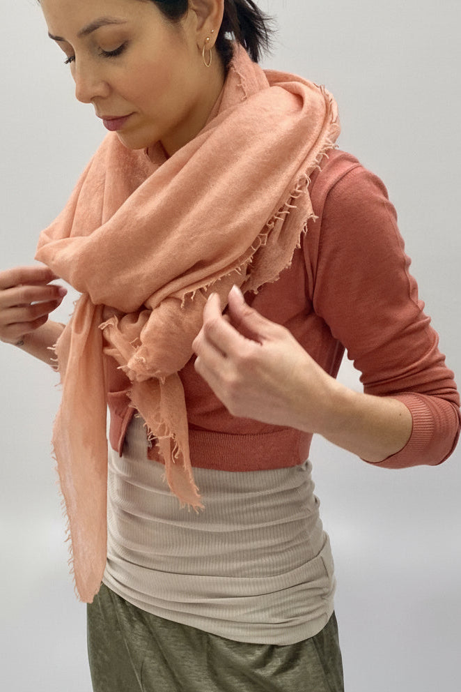 Woman wearing a pink scarf and brown sweater against a plain background