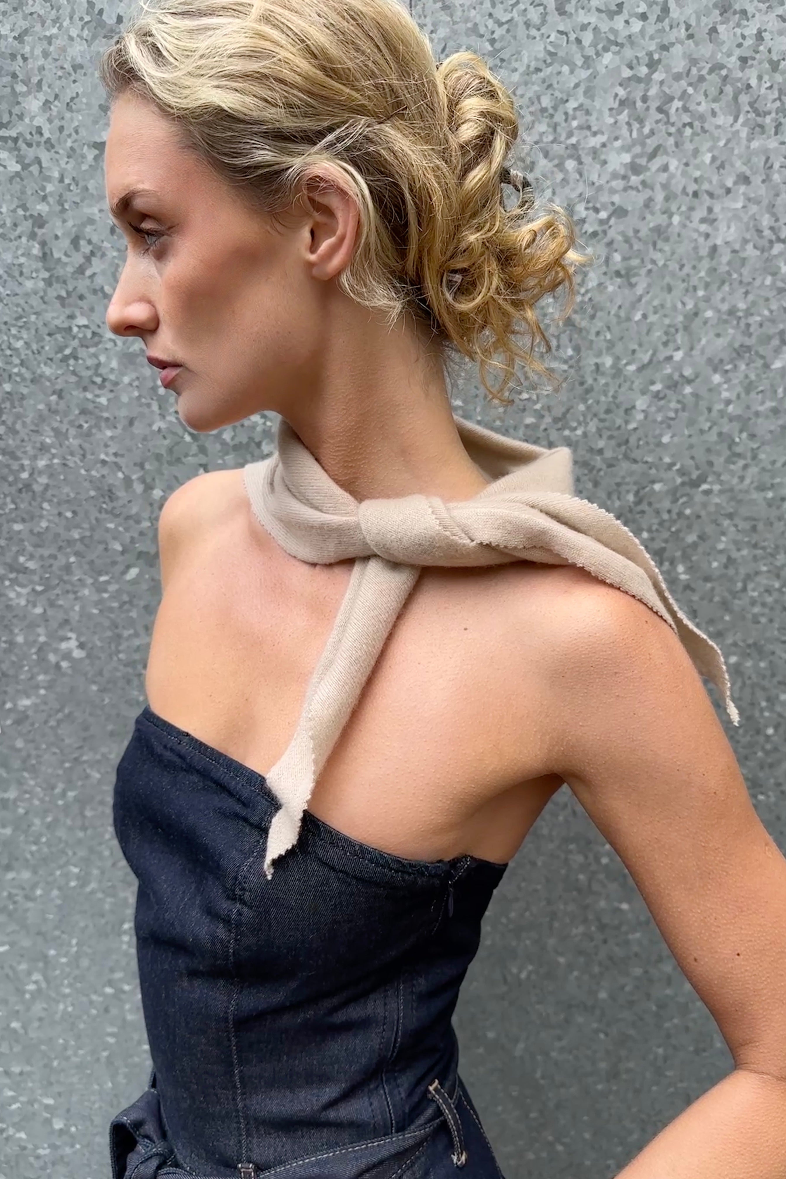 Woman wearing a strapless dark blue dress with a beige doon cashmere scarf over her shoulder against a gray background