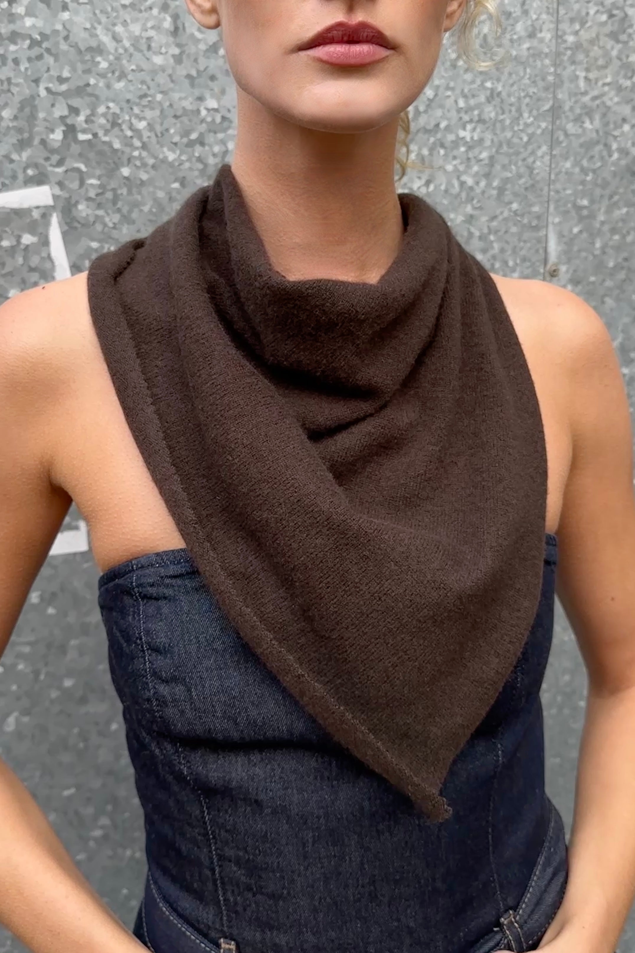 Woman wearing a doon cashmere brown scarf over a dark blue top against a gray background