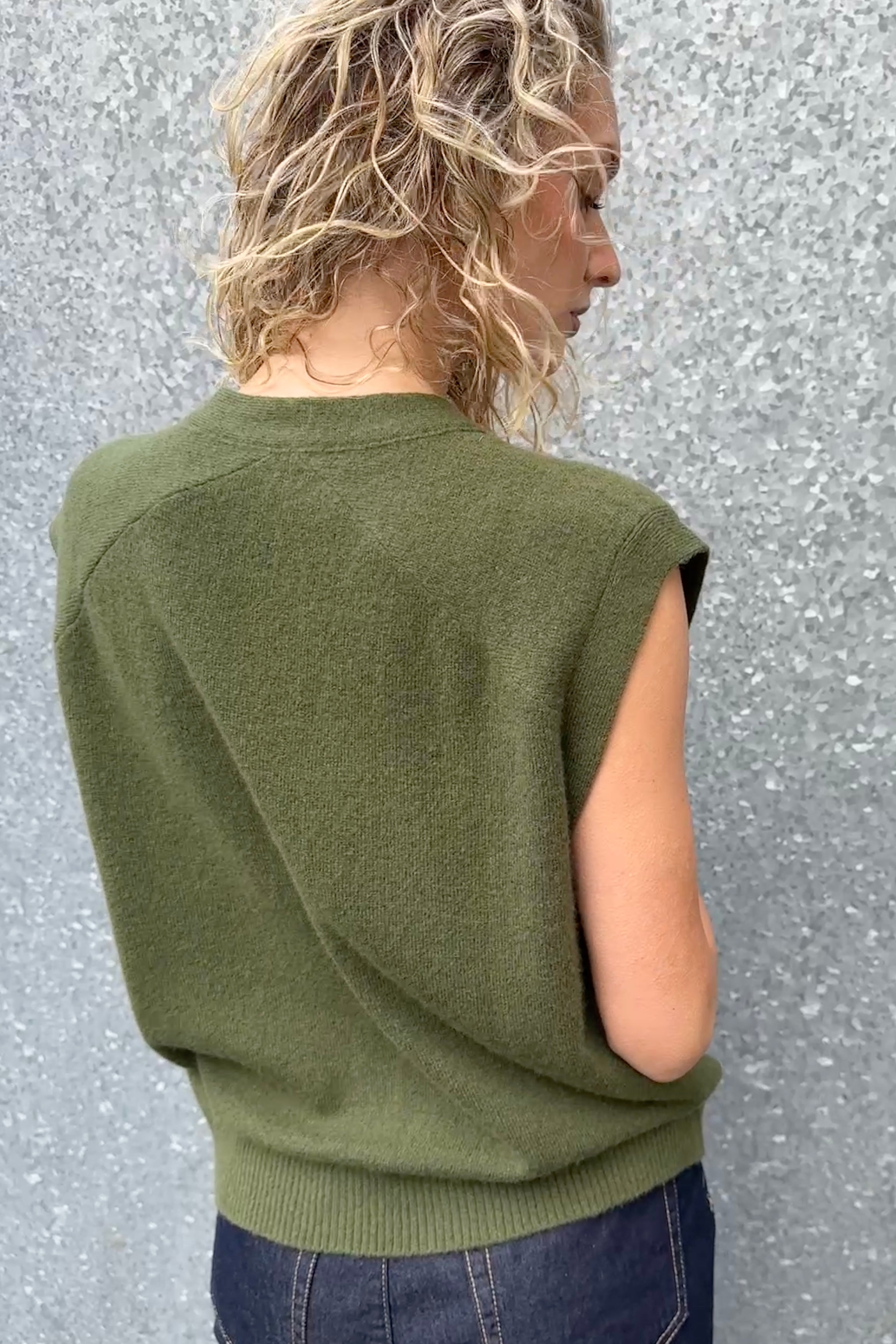 Person wearing a green sleeveless sweater against a textured gray background