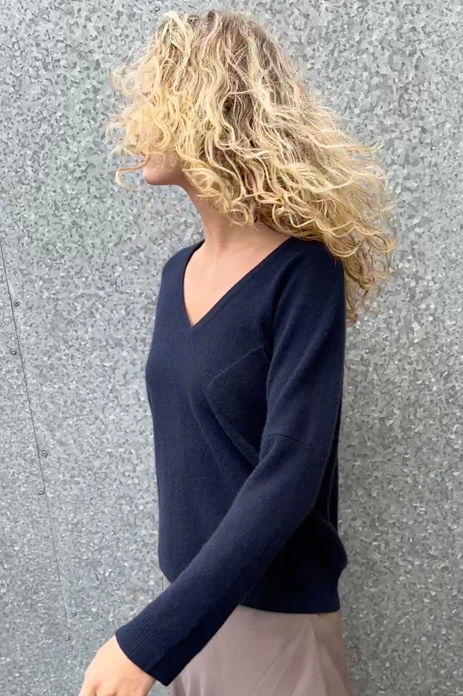 model wearing a navy blue v neck sweater against a gray wall