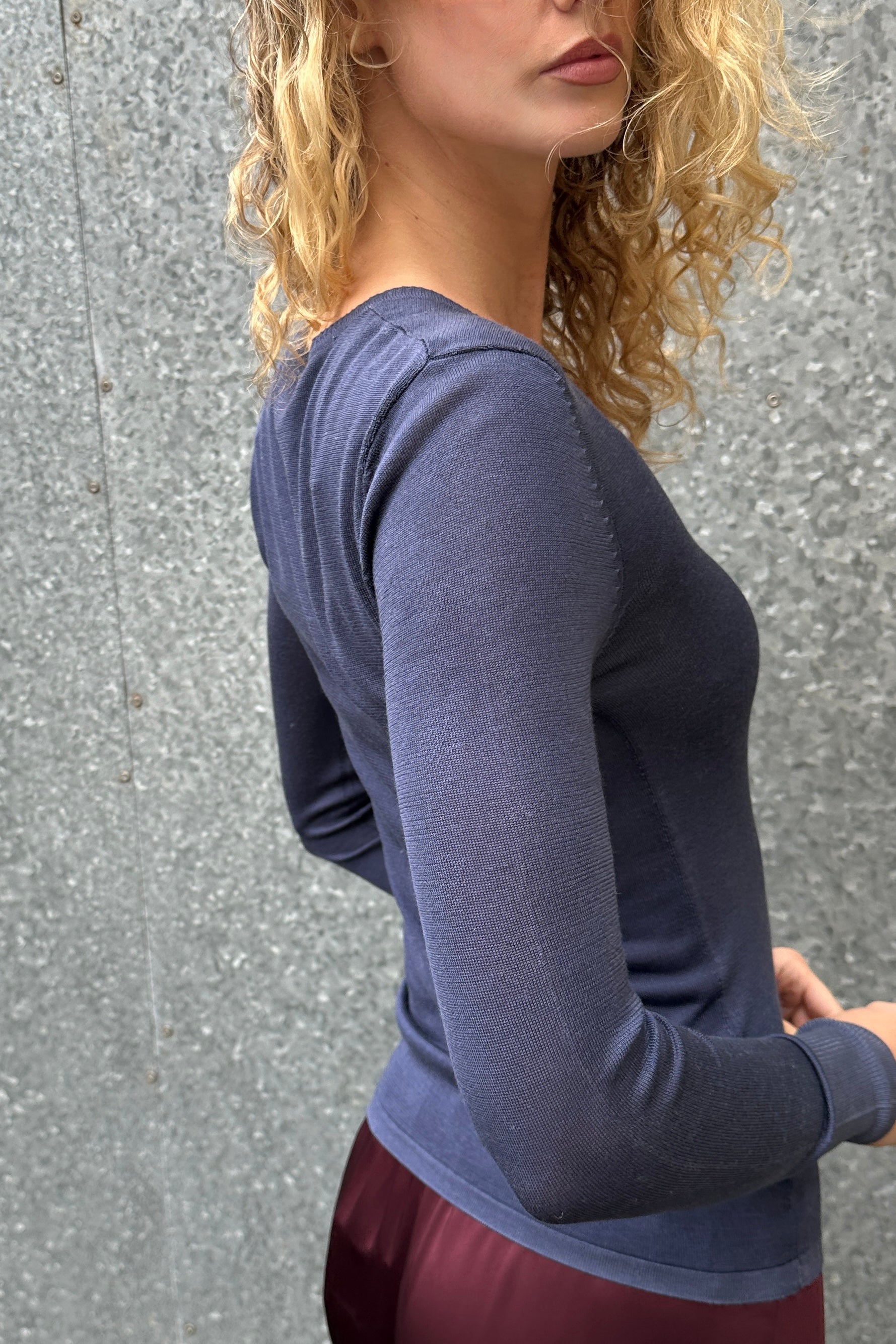 Woman wearing a blue long-sleeve top against a gray wall side view