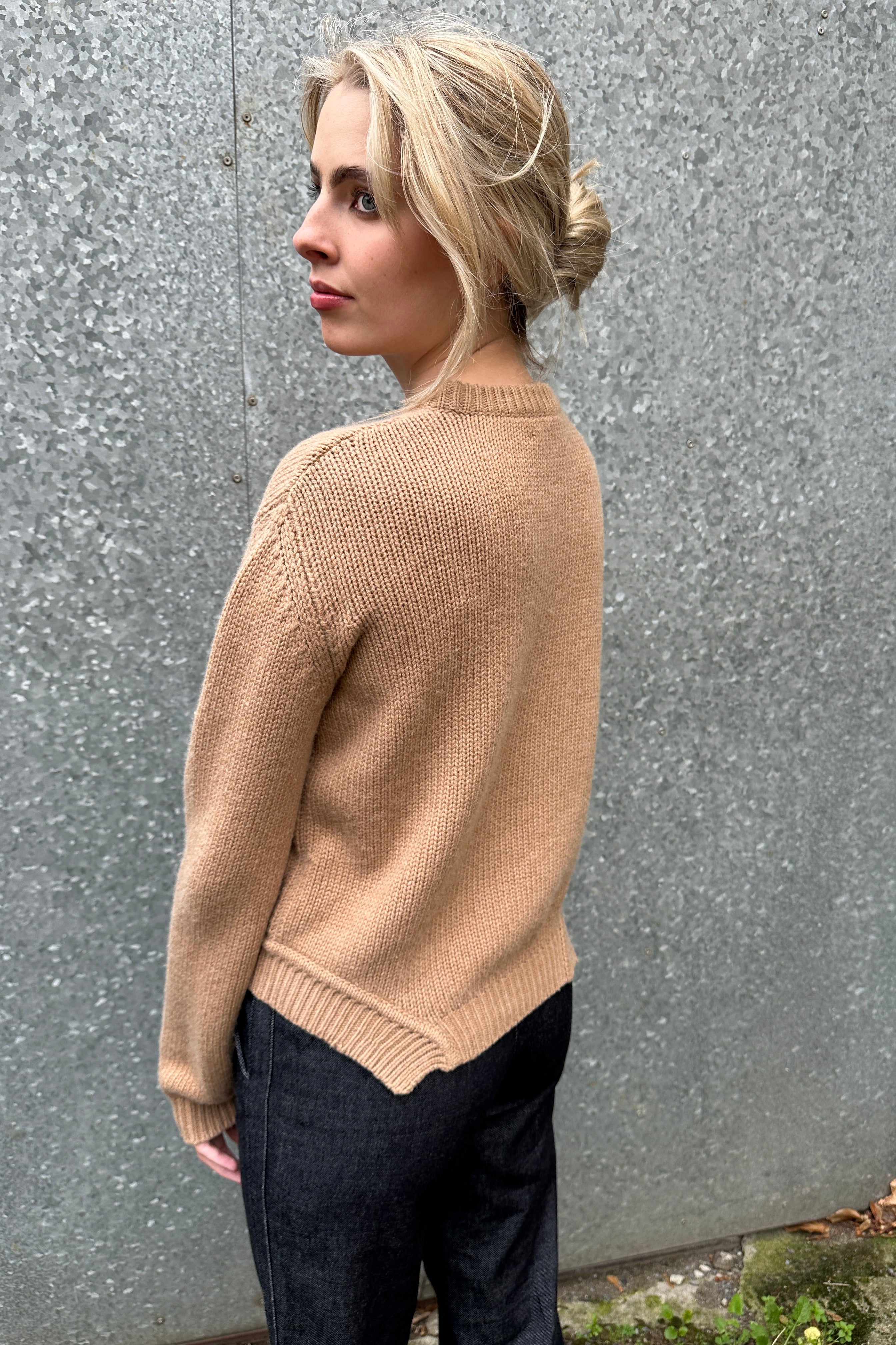 Person wearing a beige sweater and black pants on a road side view