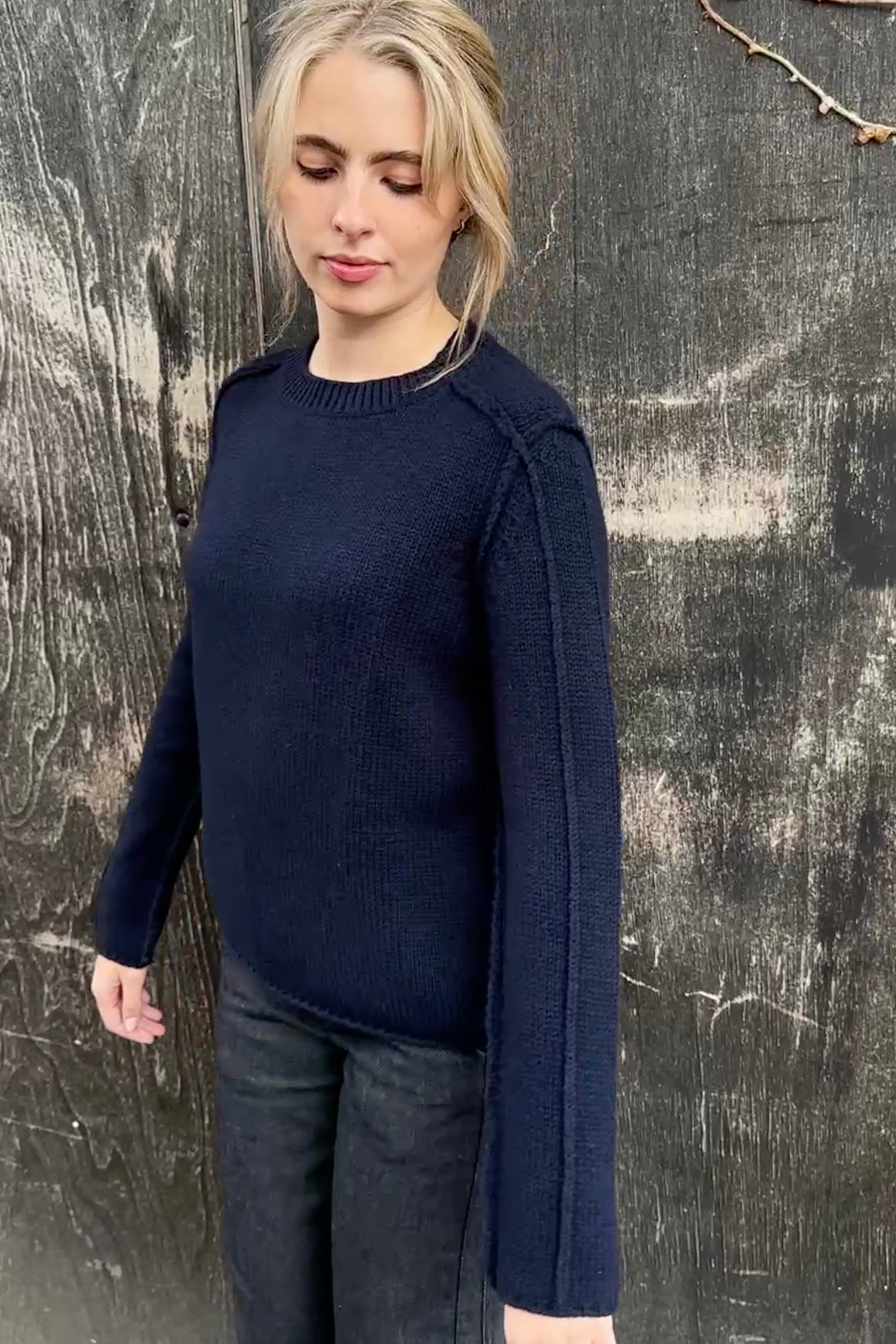 Woman wearing a navy sweater against a textured wooden wall