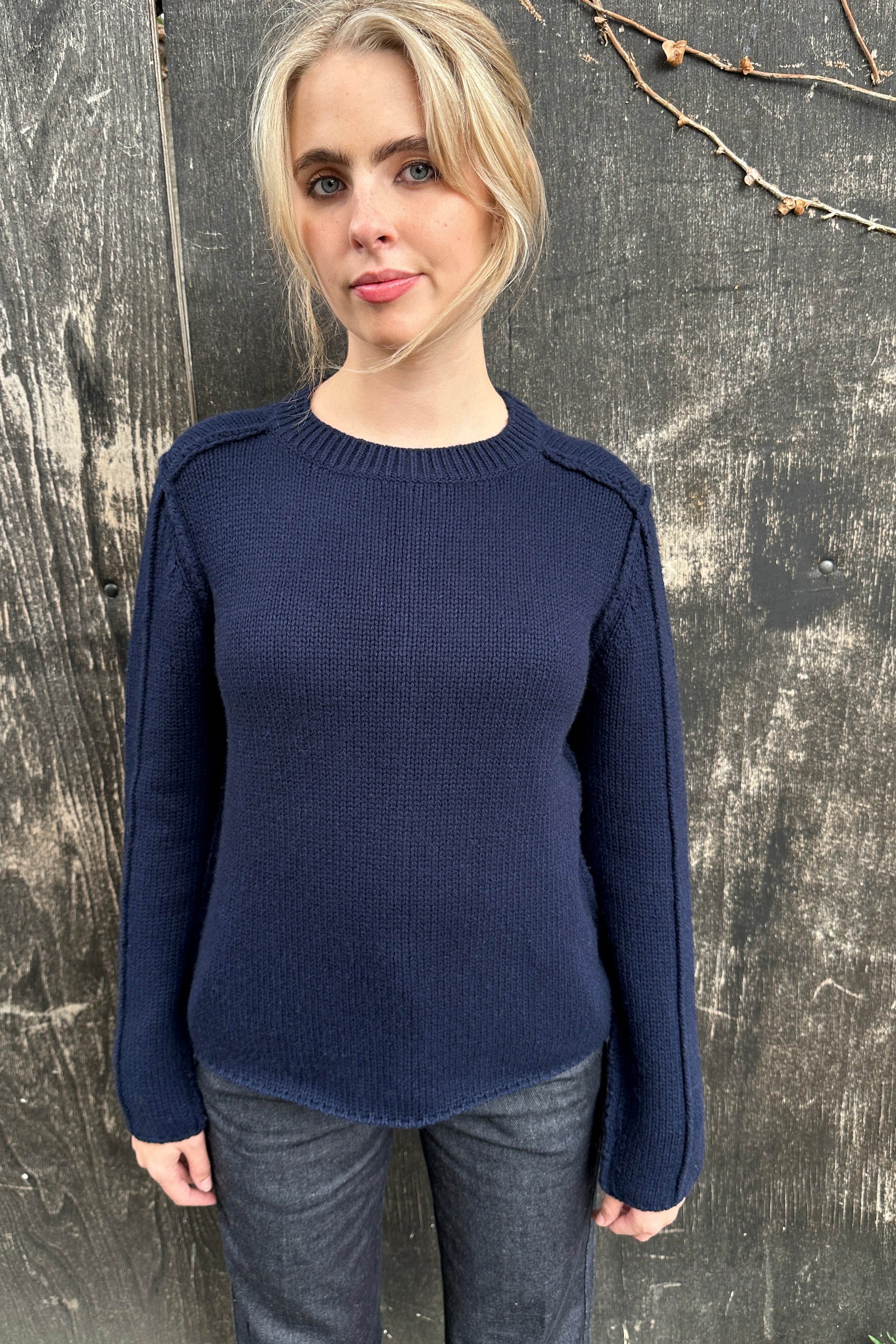 Woman wearing a navy blue sweater against a textured wall.