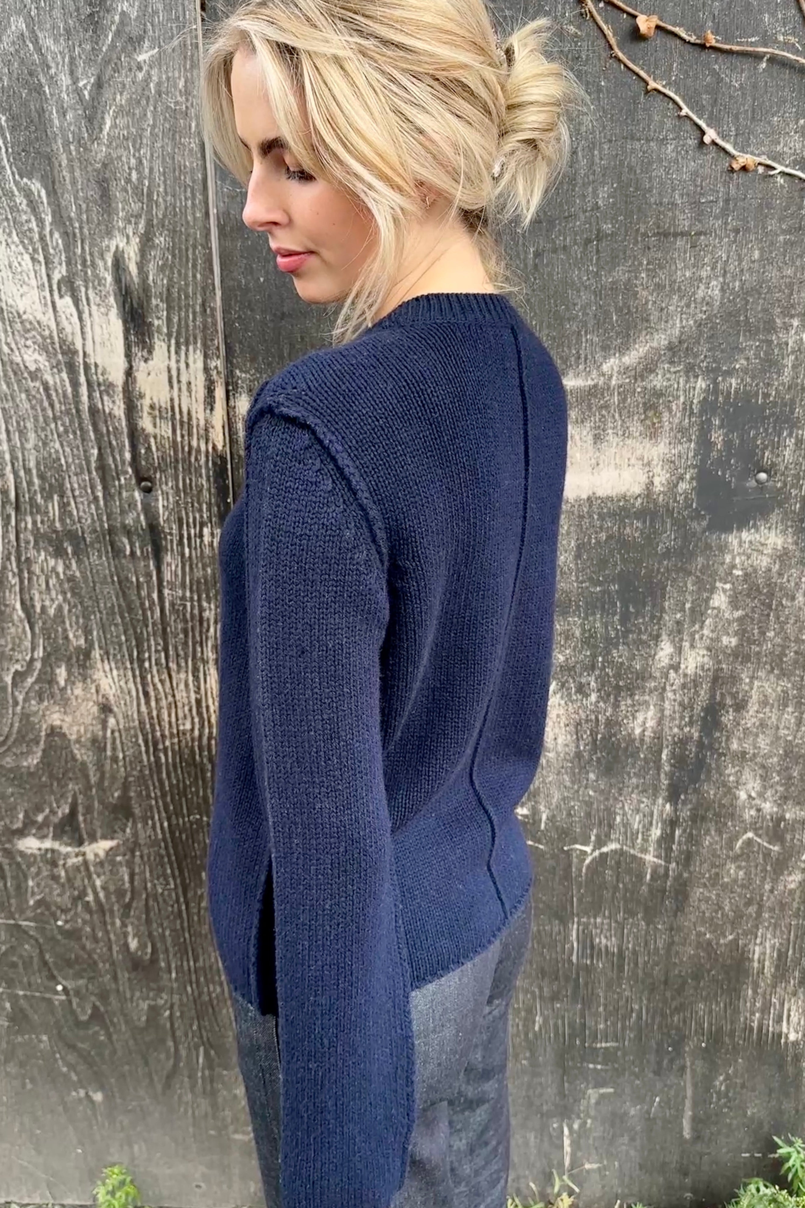 Woman wearing a blue sweater standing against a textured wall.