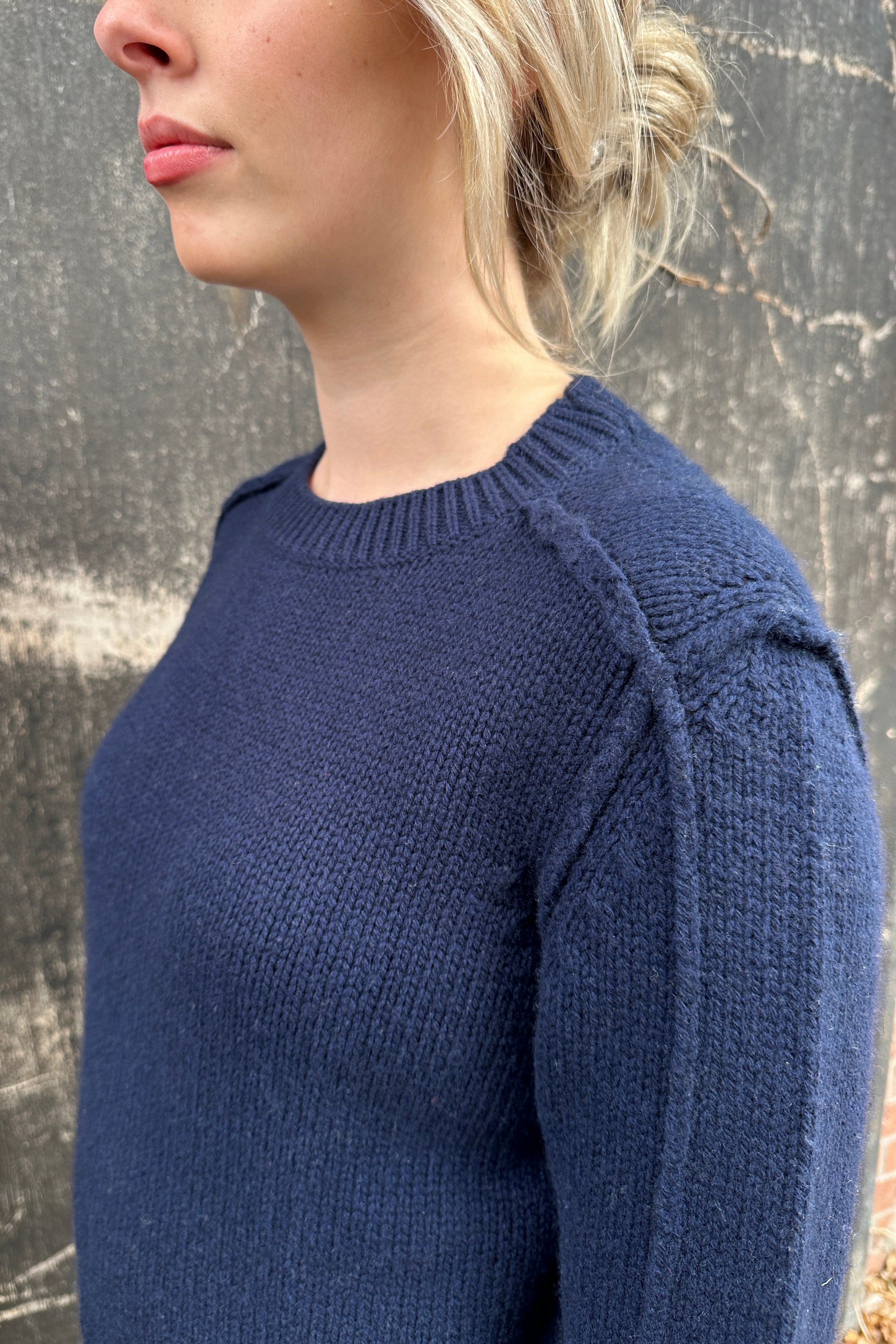 Person wearing a blue knitted sweater against a textured wall.