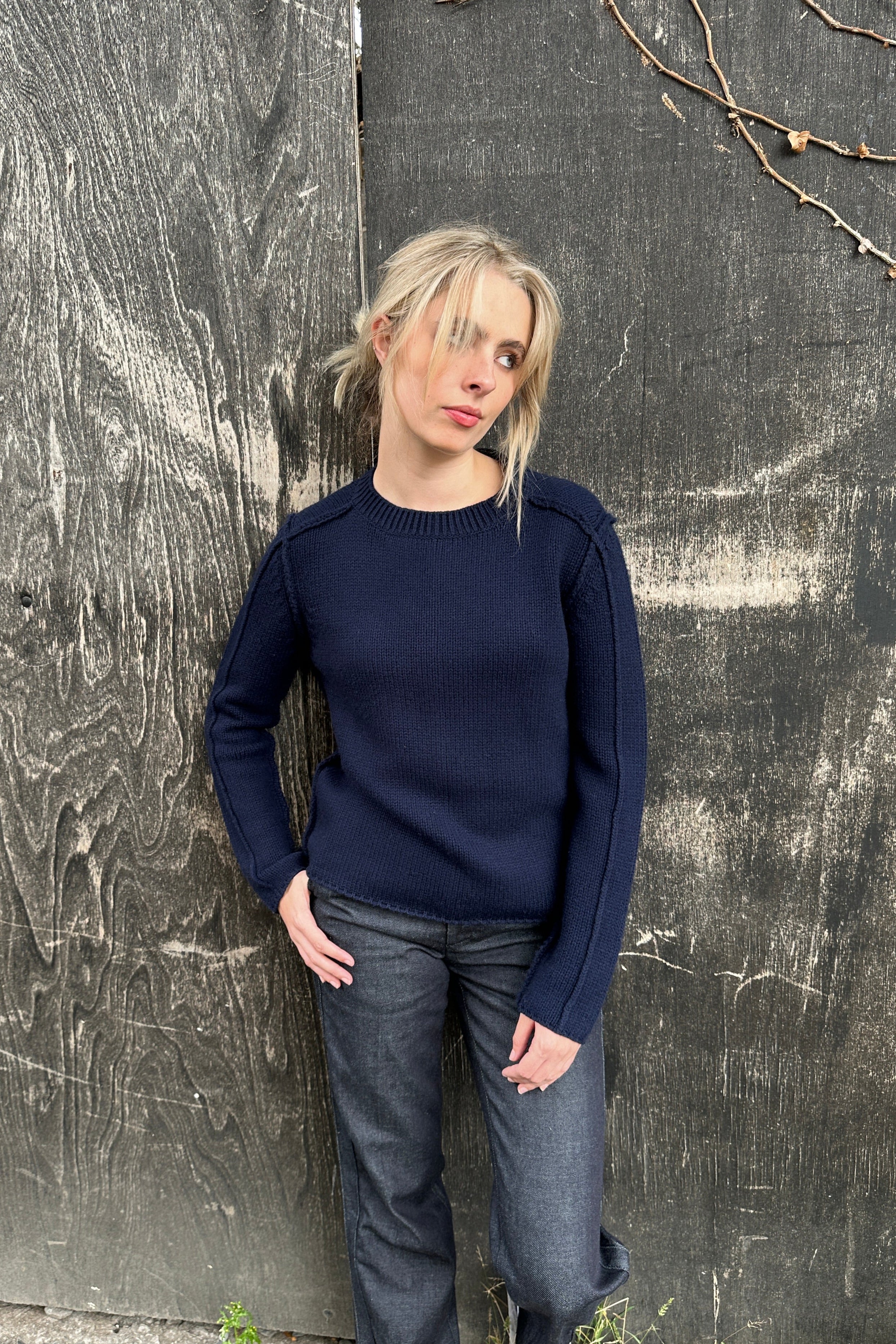 woman leaning against a wall in a navy Rizzo sweater