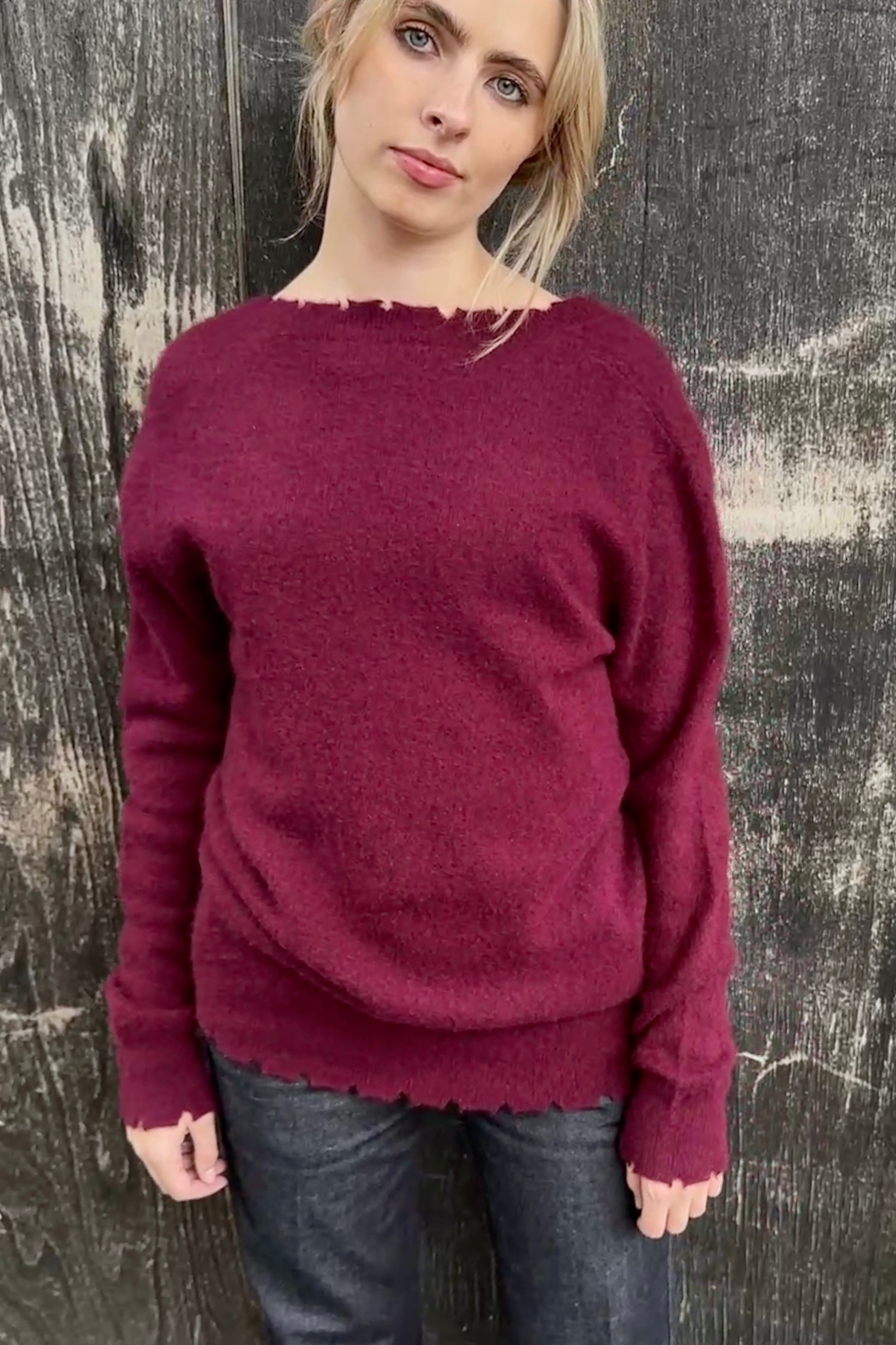 Woman wearing a burgundy sweater against a textured wall.