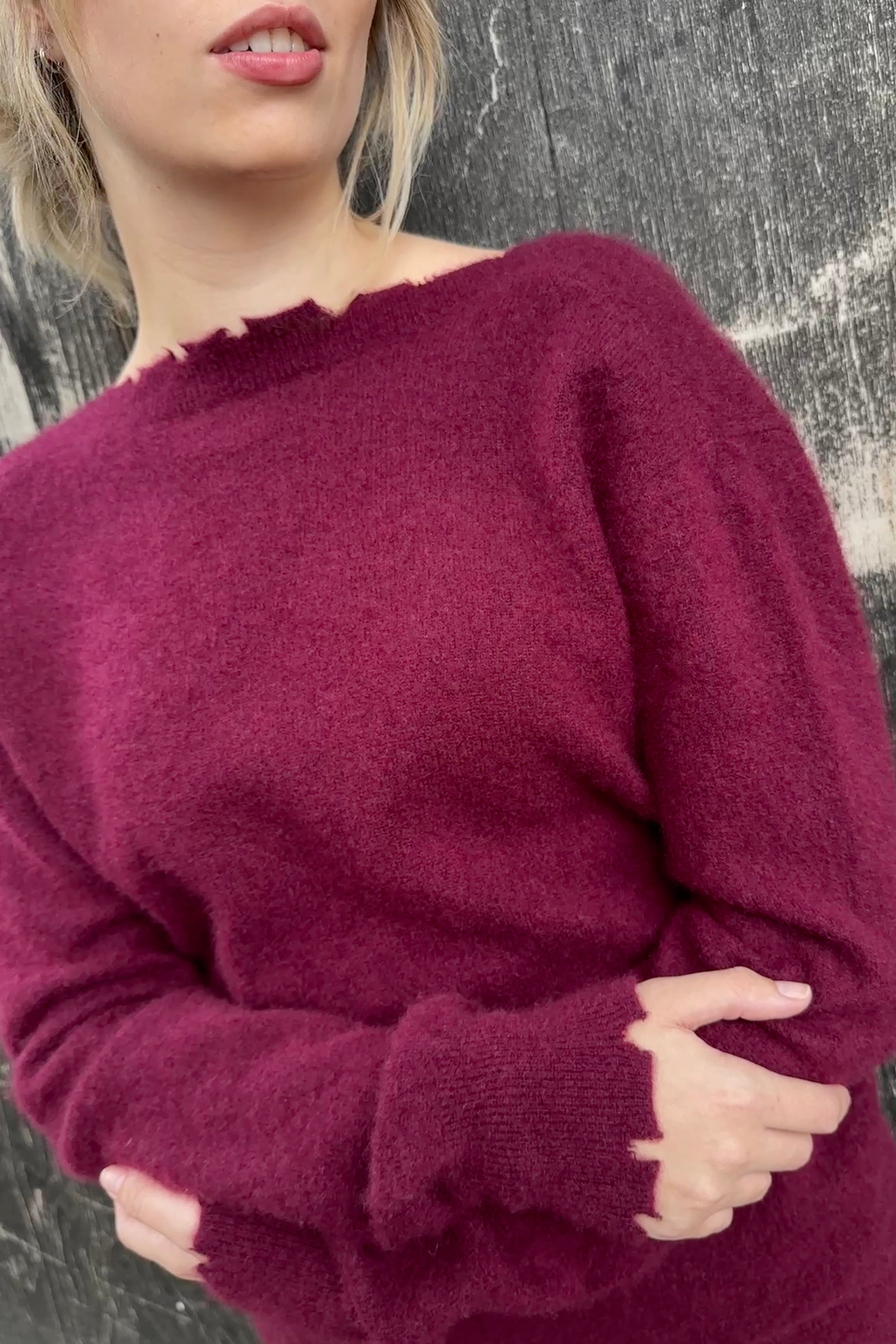 Person wearing a burgundy sweater against a textured gray background