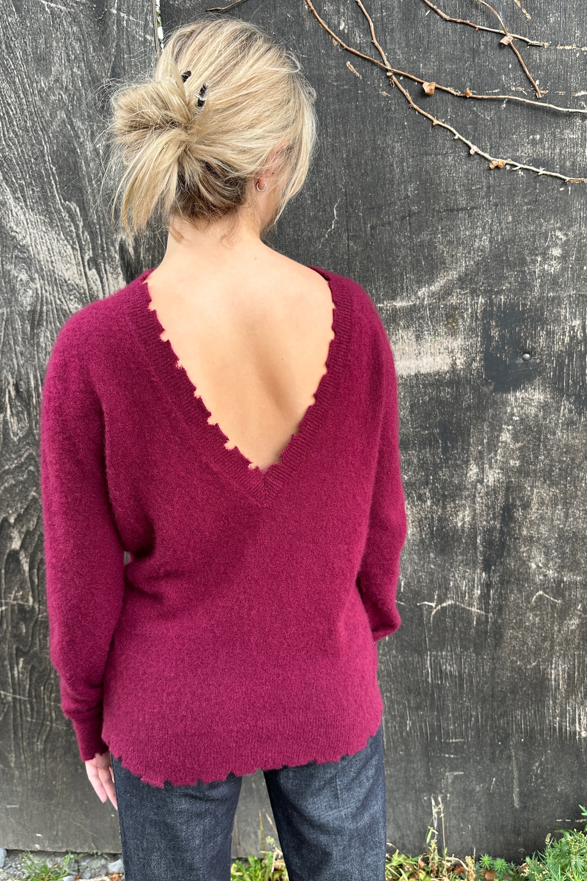 Person wearing a maroon sweater with an open back against a textured wall.