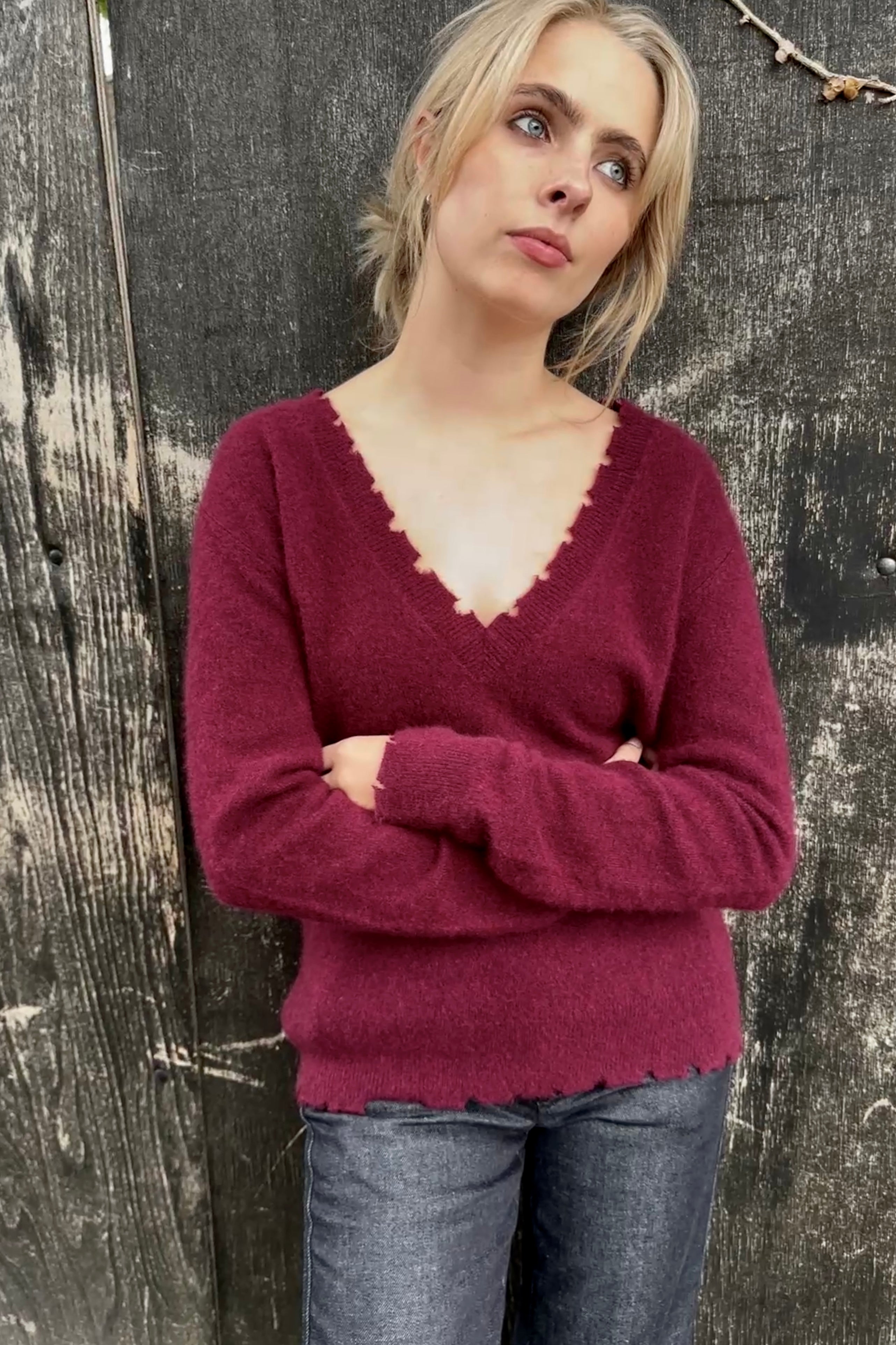 Woman wearing a burgundy sweater and blue jeans against a textured wall.