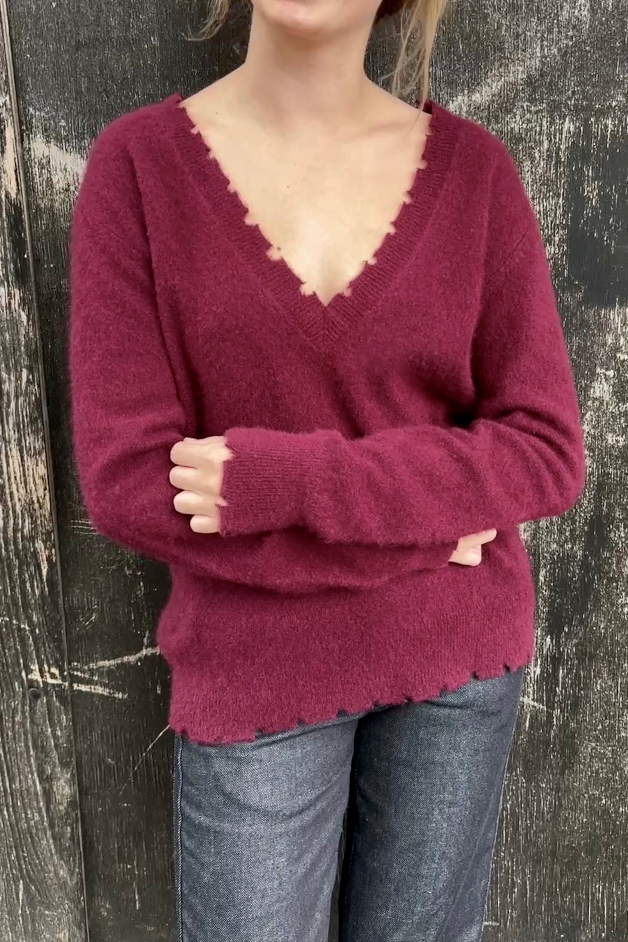 Person wearing a burgundy sweater with a V-neck against a dark wooden background