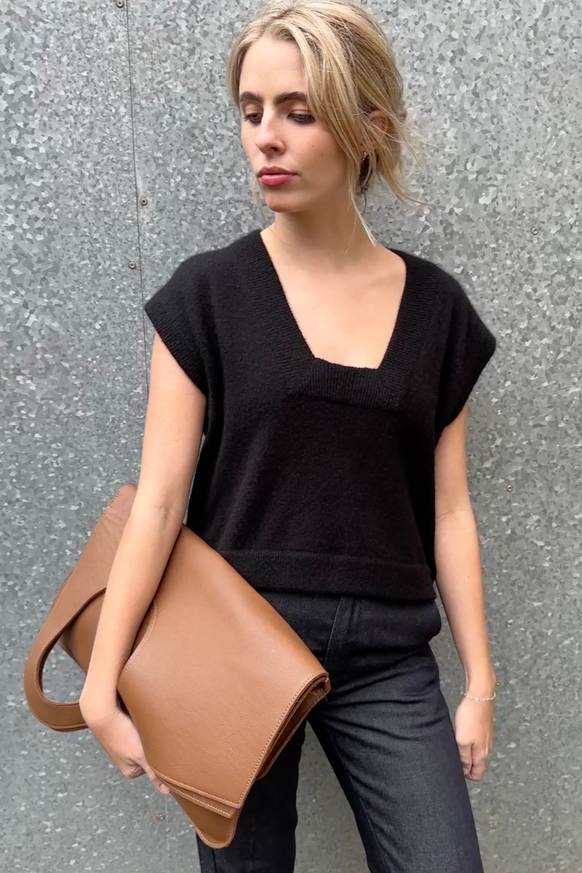 Woman wearing square neck cashmere silk inka tank top in black holding a brown leather bag against a gray wall