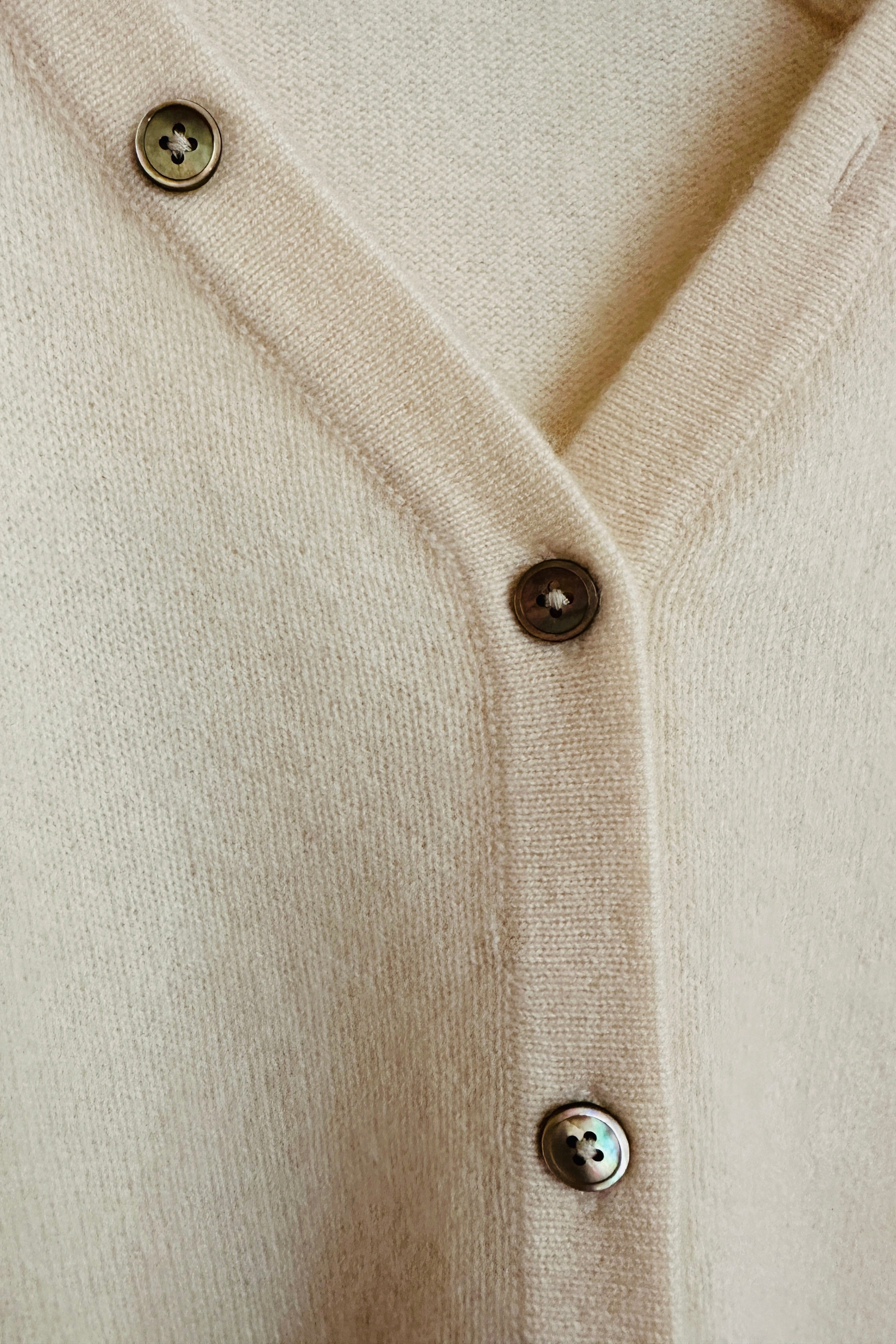Close-up of a cream zelia cardigan with buttons on a neutral background