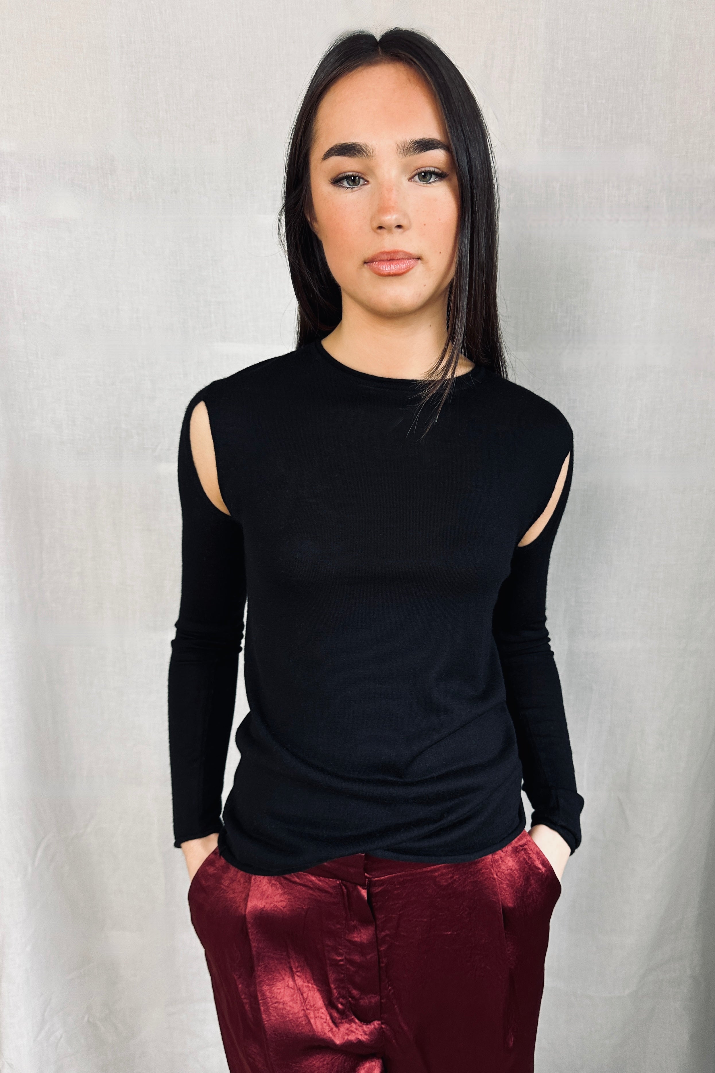 Model wearing a Richielu black long-sleeve top with cut-out design and red pants