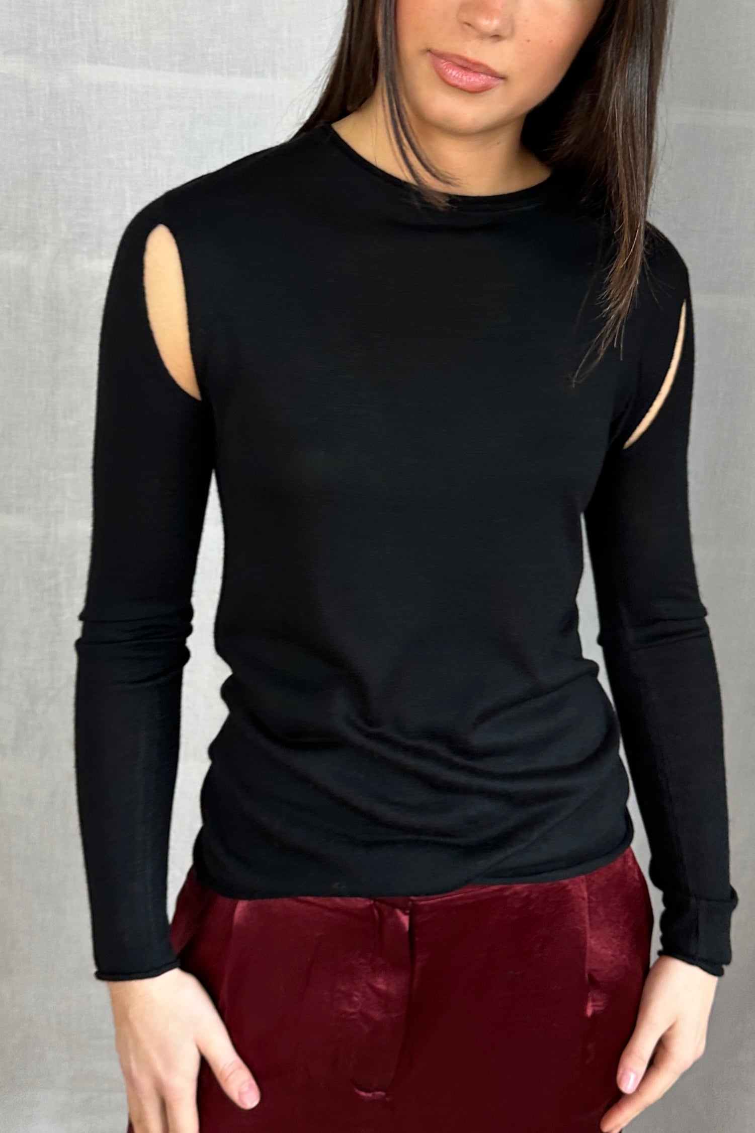 Model wearing a Richielu black long-sleeve top with cut-out design and red pants 2