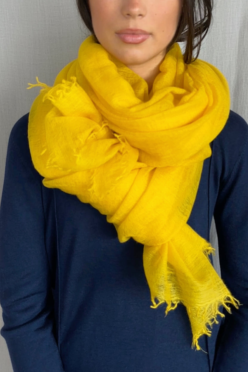 model wearing a bright mustard yellow scarf over a dark blue sweater against a neutral background