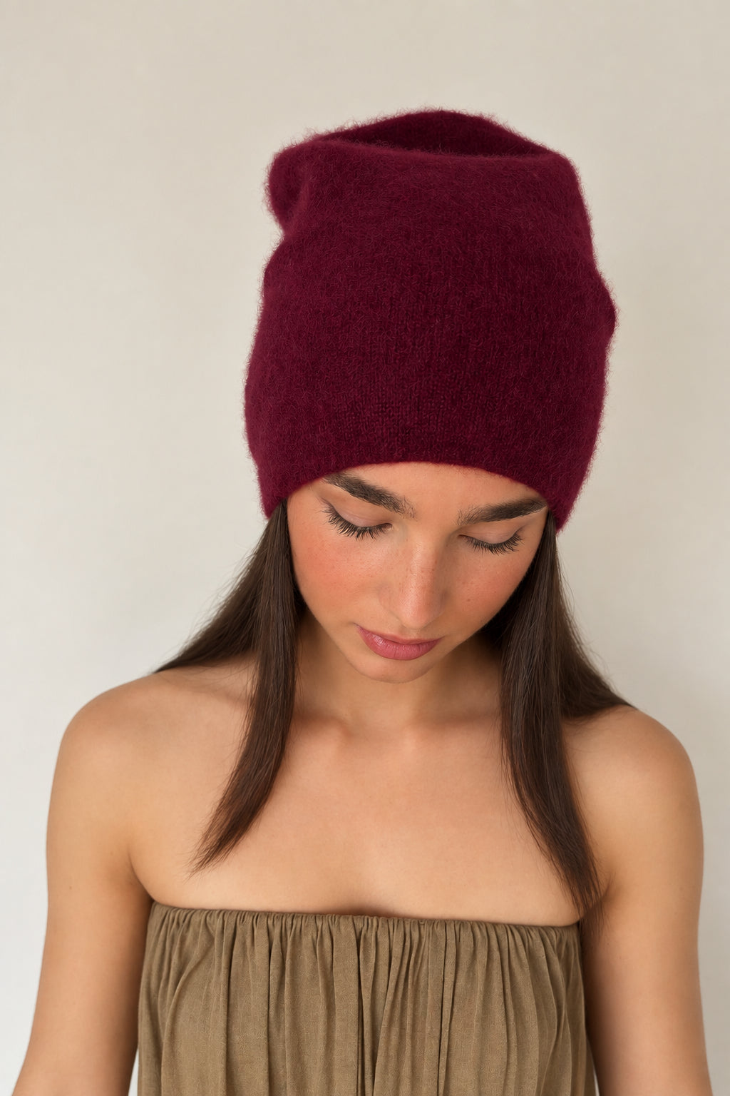 Woman wearing a burgundy knit beanie against a plain background