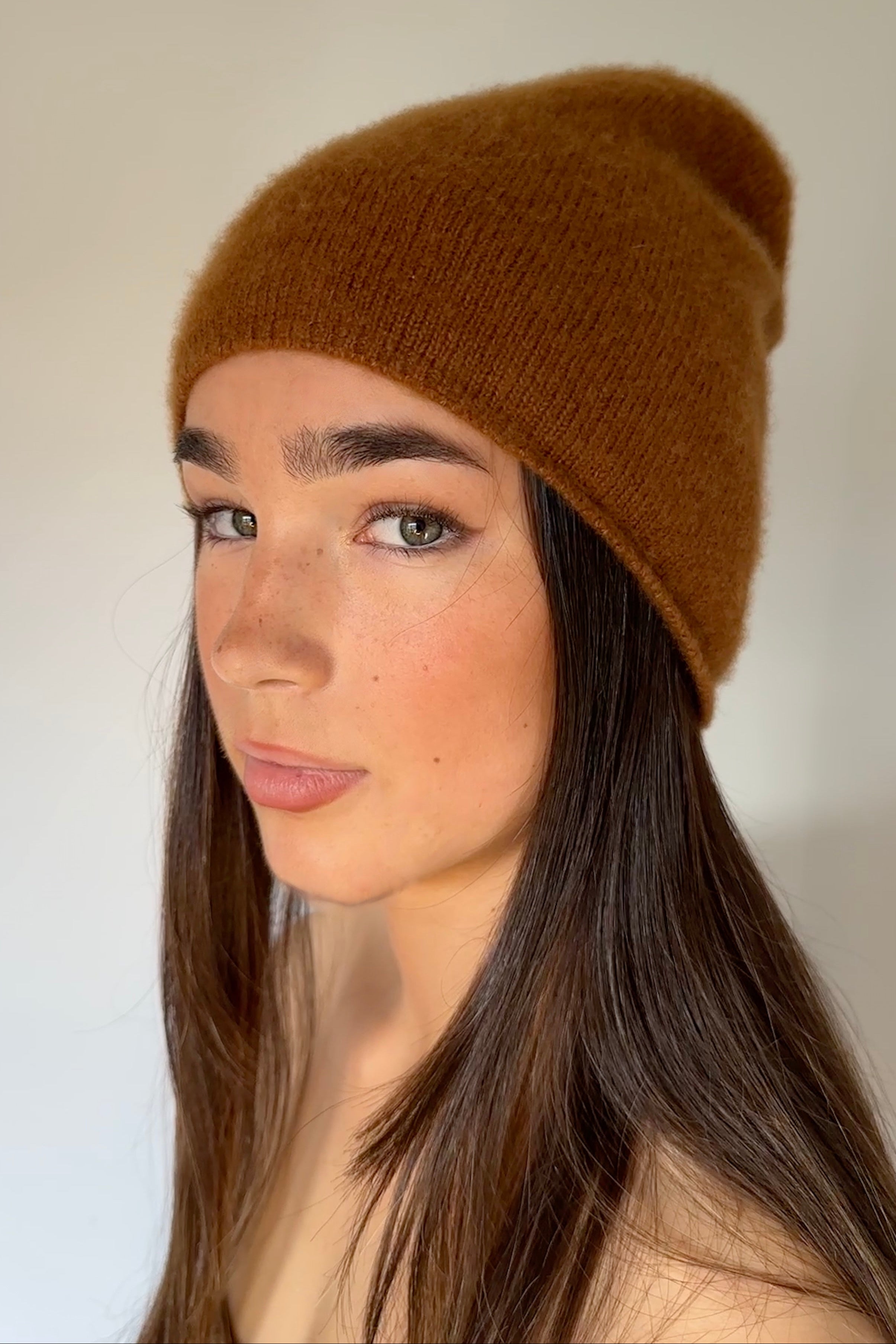 Woman wearing a beety brown knit cashmere silkl beanie against a plain background