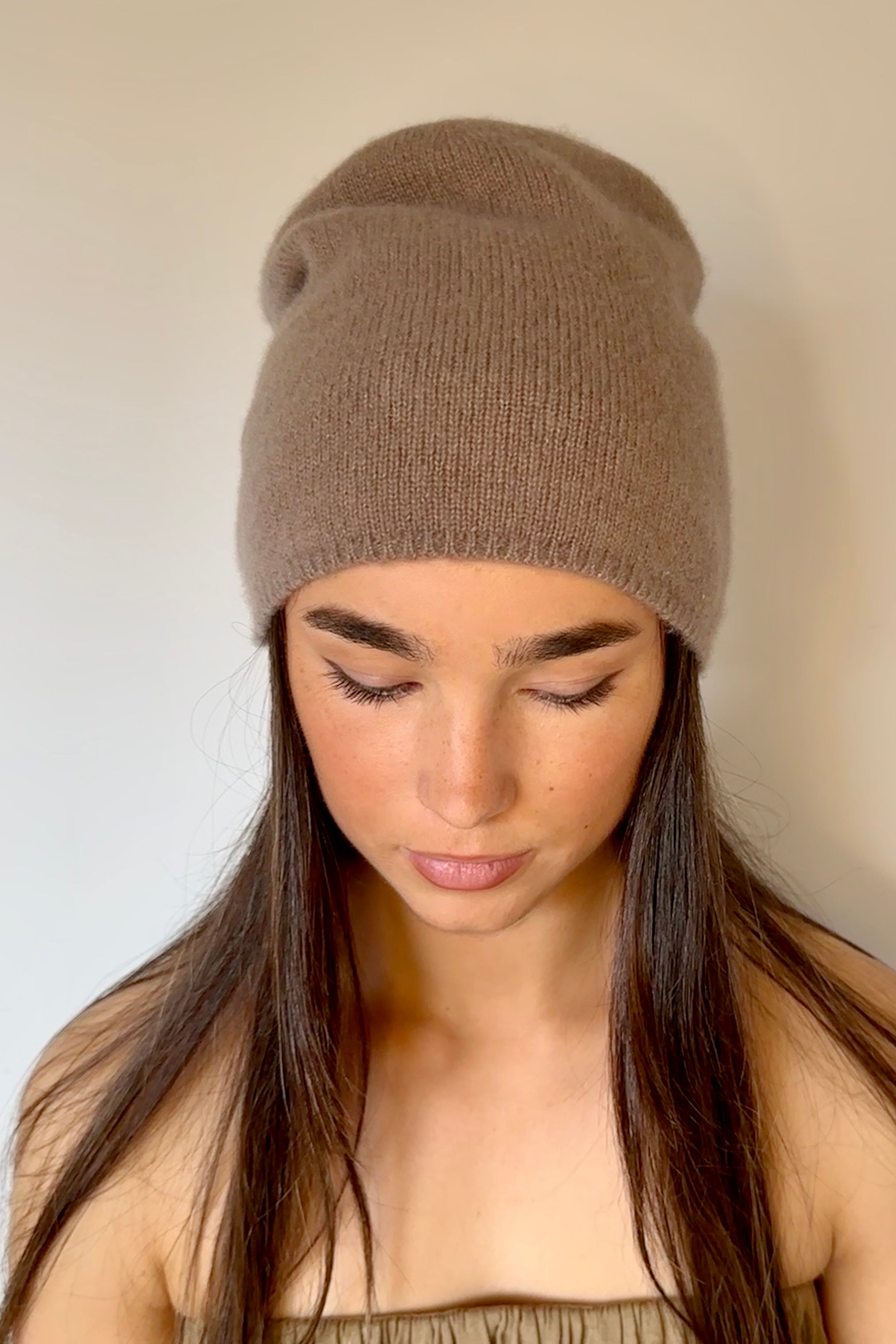 Woman wearing a beety brown knit cashmere silkl beanie against a plain background