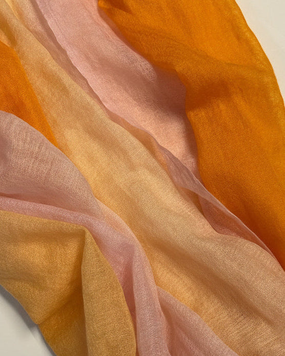 Close-up of cashmere ombre scarf fabric with orange, pink, and peach colors on a white background