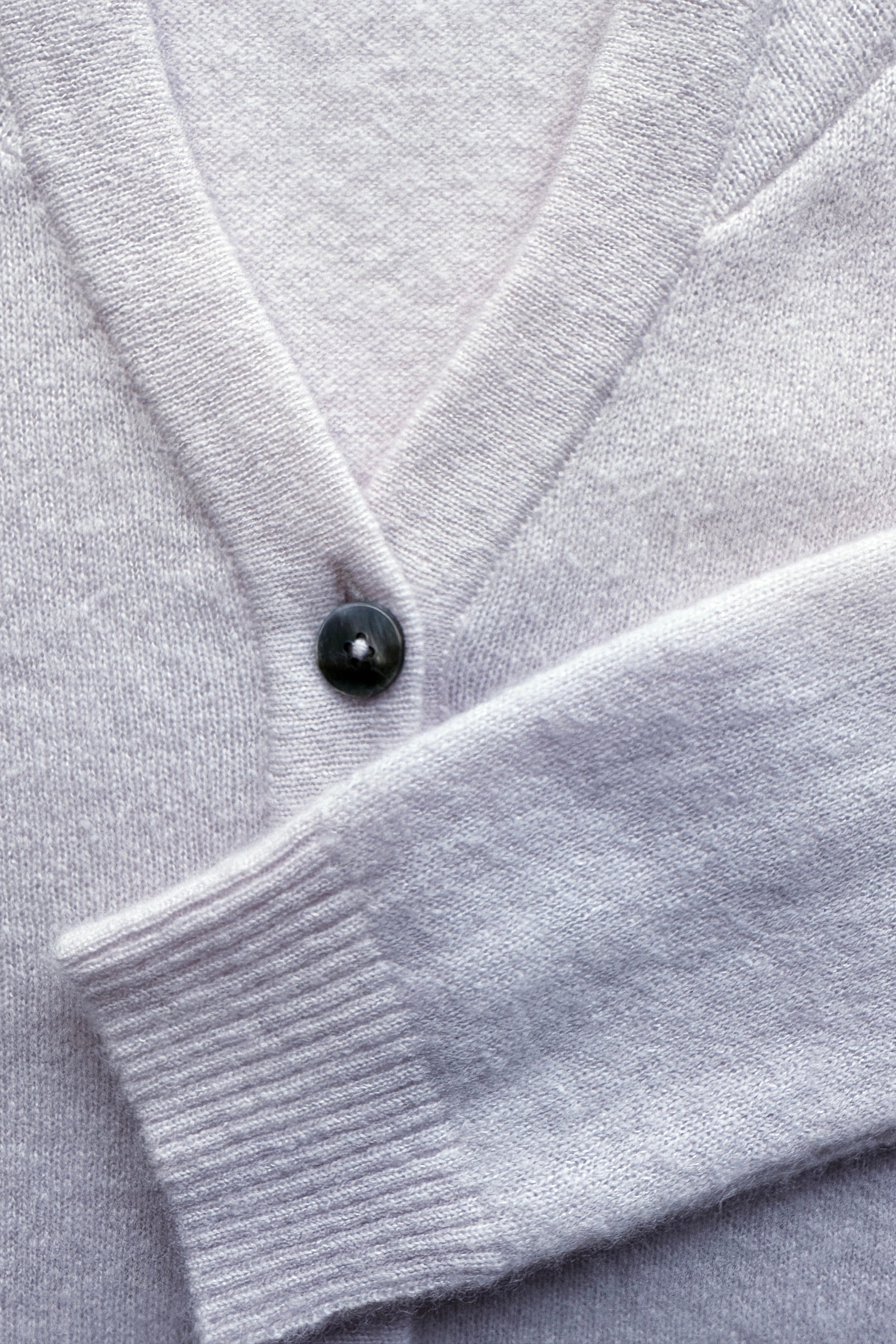Close-up of a violet cardigan with a black button on a matching fabric background