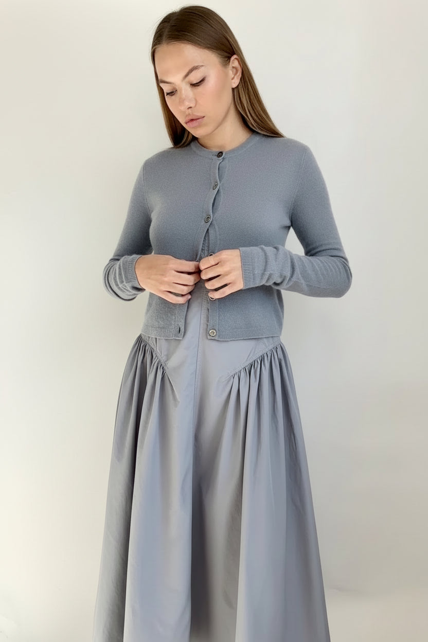 Woman wearing a gray cardigan and skirt set against a plain background