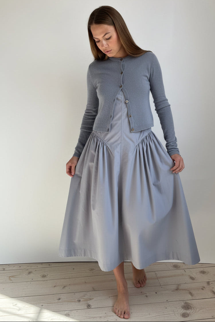 Woman wearing a long-sleeve cashmere cardigan in blue grey steel and matching skirt against a white background