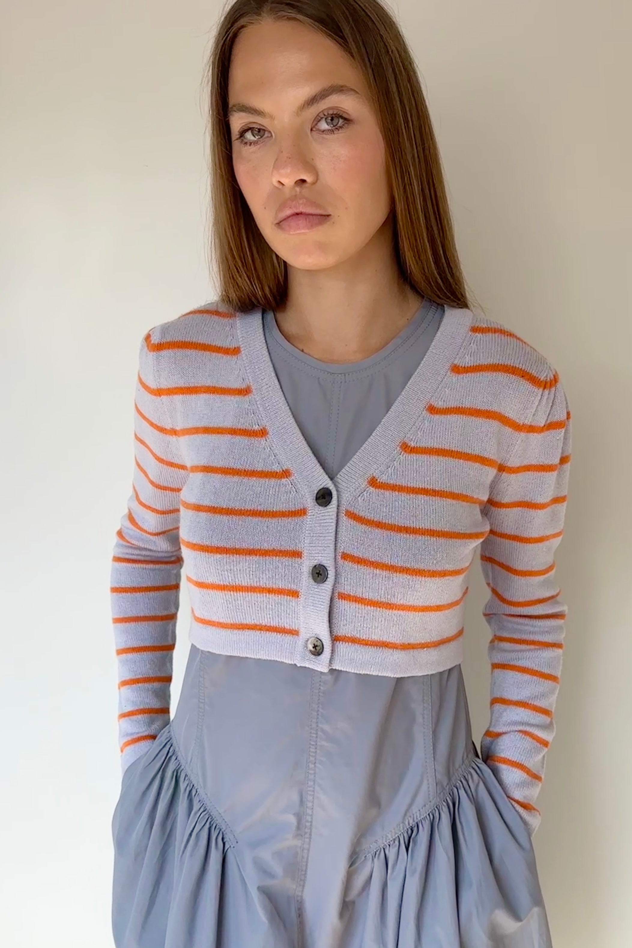 Woman wearing a striped cardigan over a gray dress with a plain background