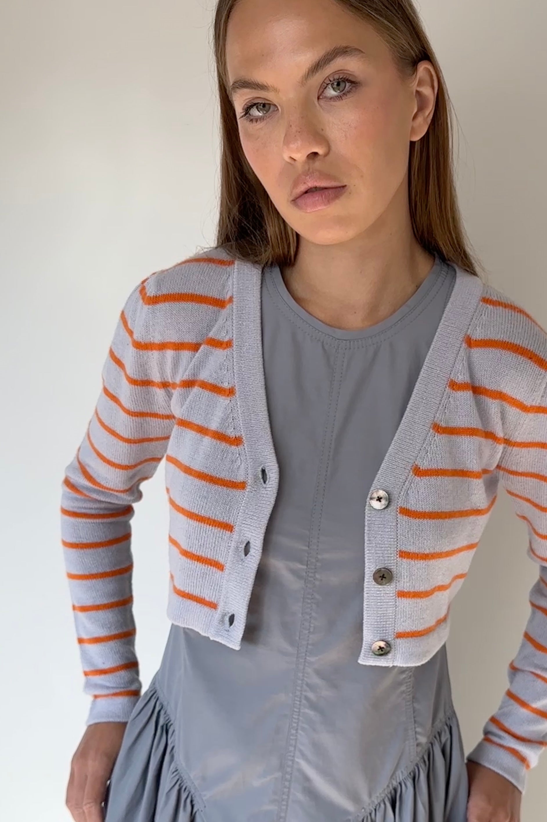 Woman wearing a gray dress with an orange and lilac striped cardigan against a plain background