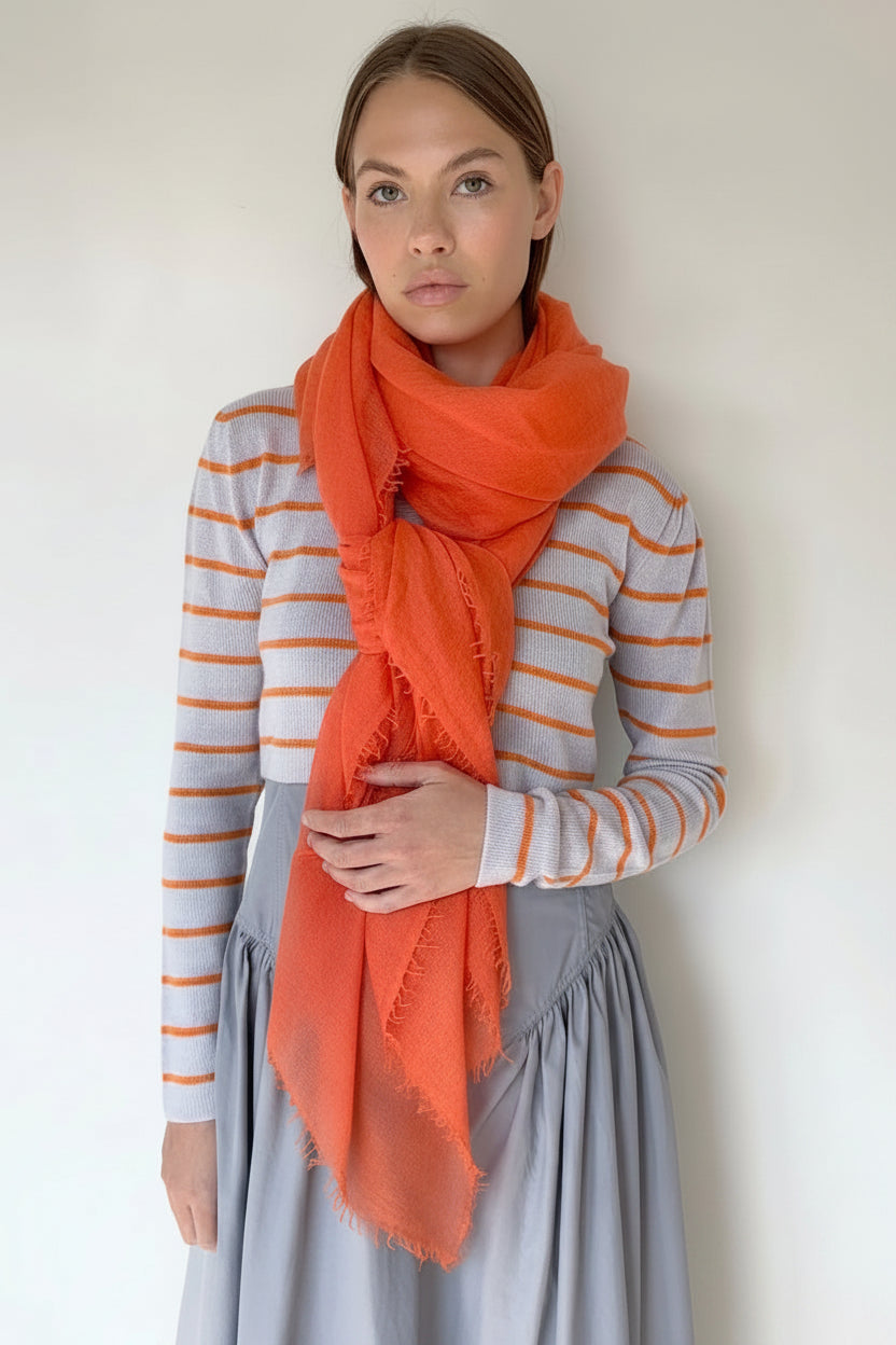 Woman wearing a striped cardi and orange scarf against a plain background