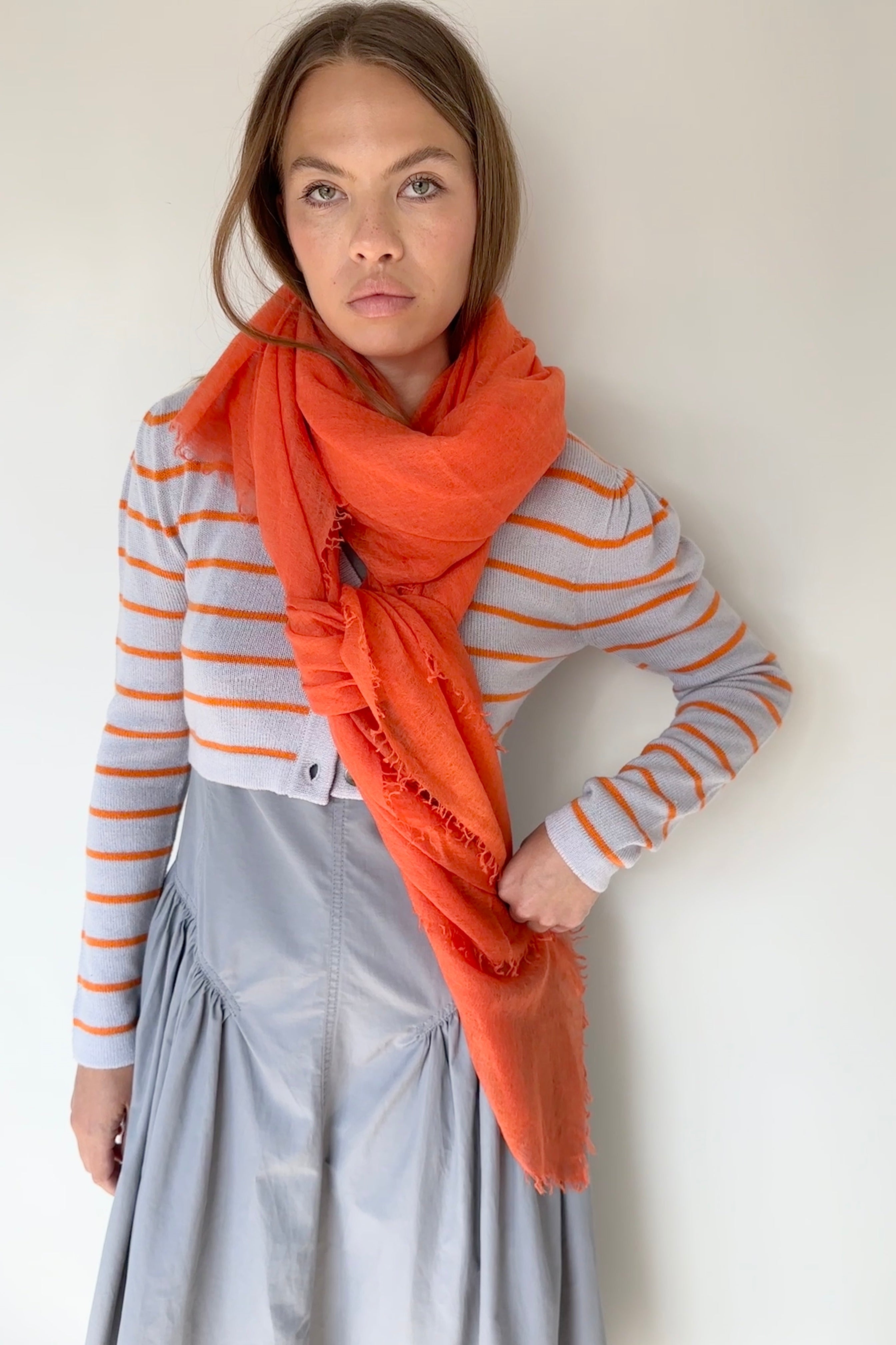 Woman wearing an orange scarf, striped sweater, and gray skirt against a white background